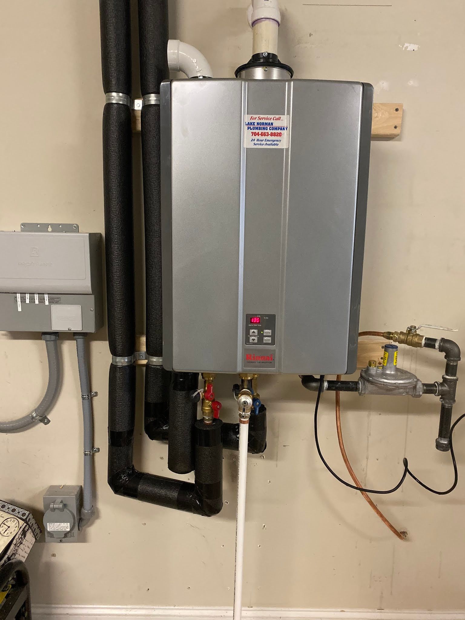 Wall-mounted silver tankless water heater with exposed pipes and control panel in a utility room