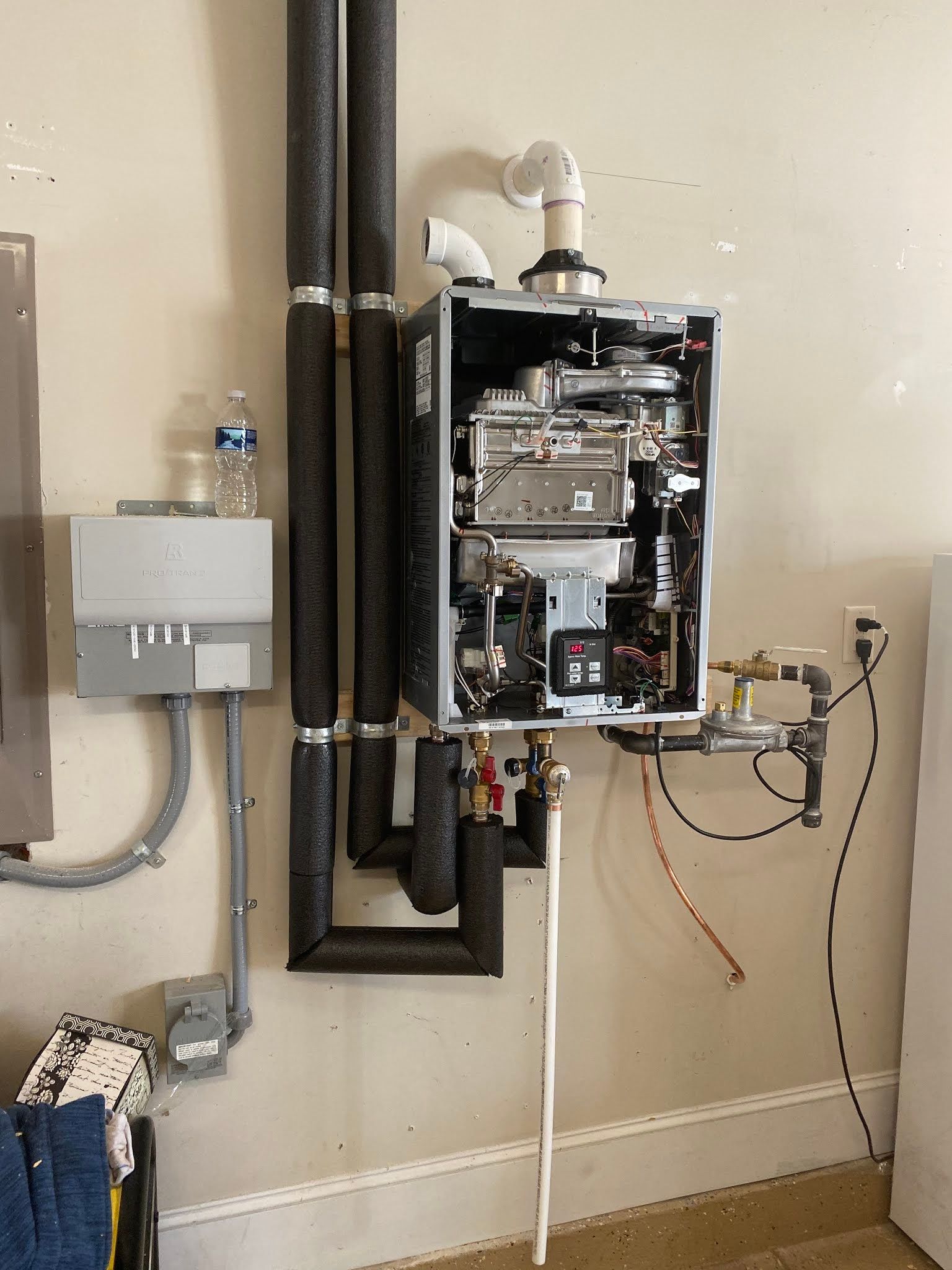 Wall-mounted gas water heater with exposed pipes and vents in a utility room.