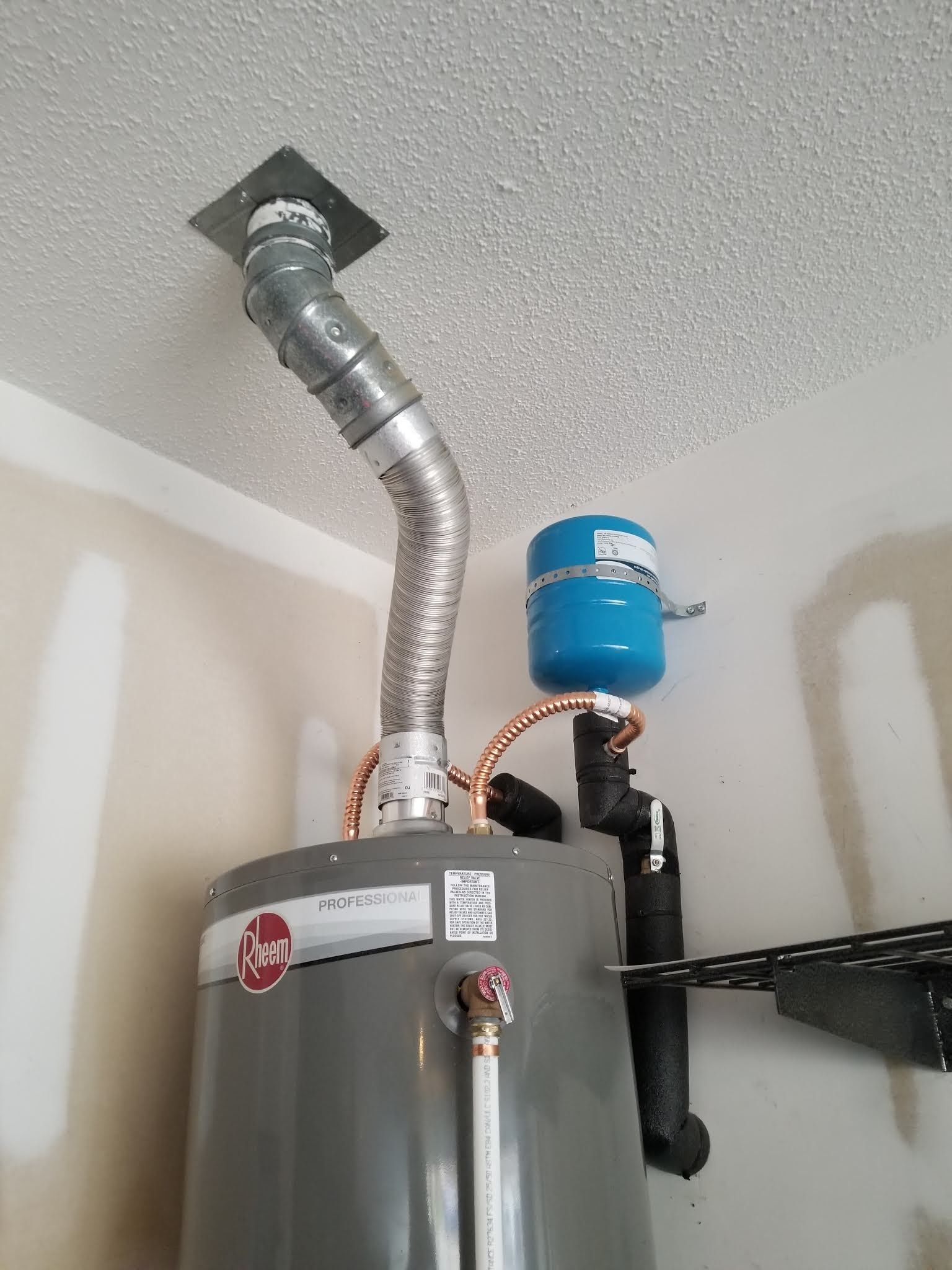 Water heater with silver vent pipe and blue expansion tank in a utility room corner