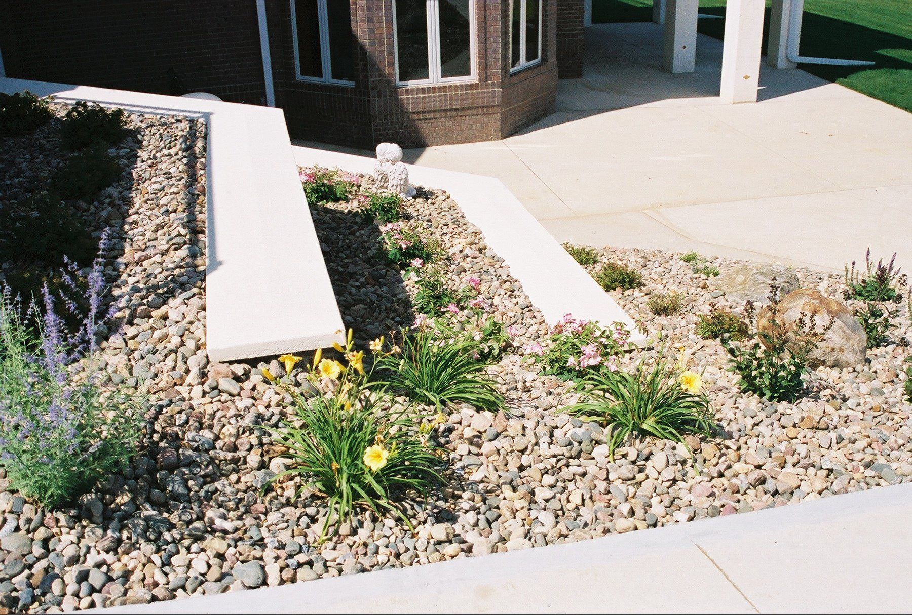 Landscaped rock garden with shrubs and white concrete steps beside a building entrance