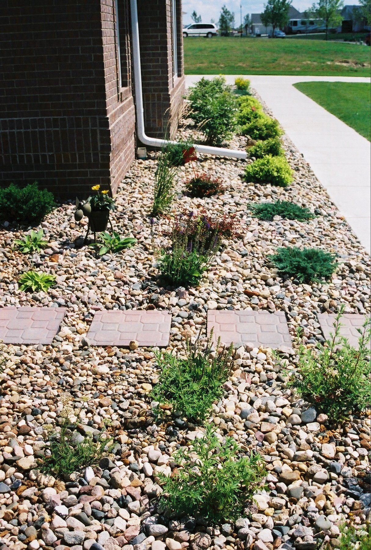 Front yard landscaping with gravel, small shrubs, stepping stones, and a walkway beside a brick house