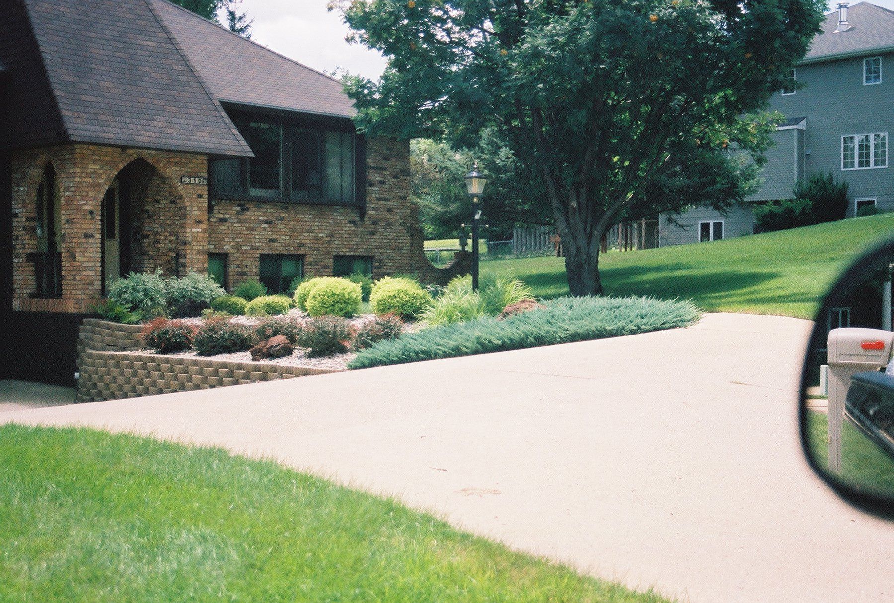 Brick house with landscaped front yard beside a curved driveway, viewed from a car window