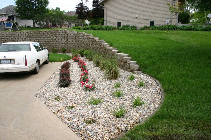 Driveway landscaped with white gravel, pink flowers, and a curved stone border beside a parked white car.
