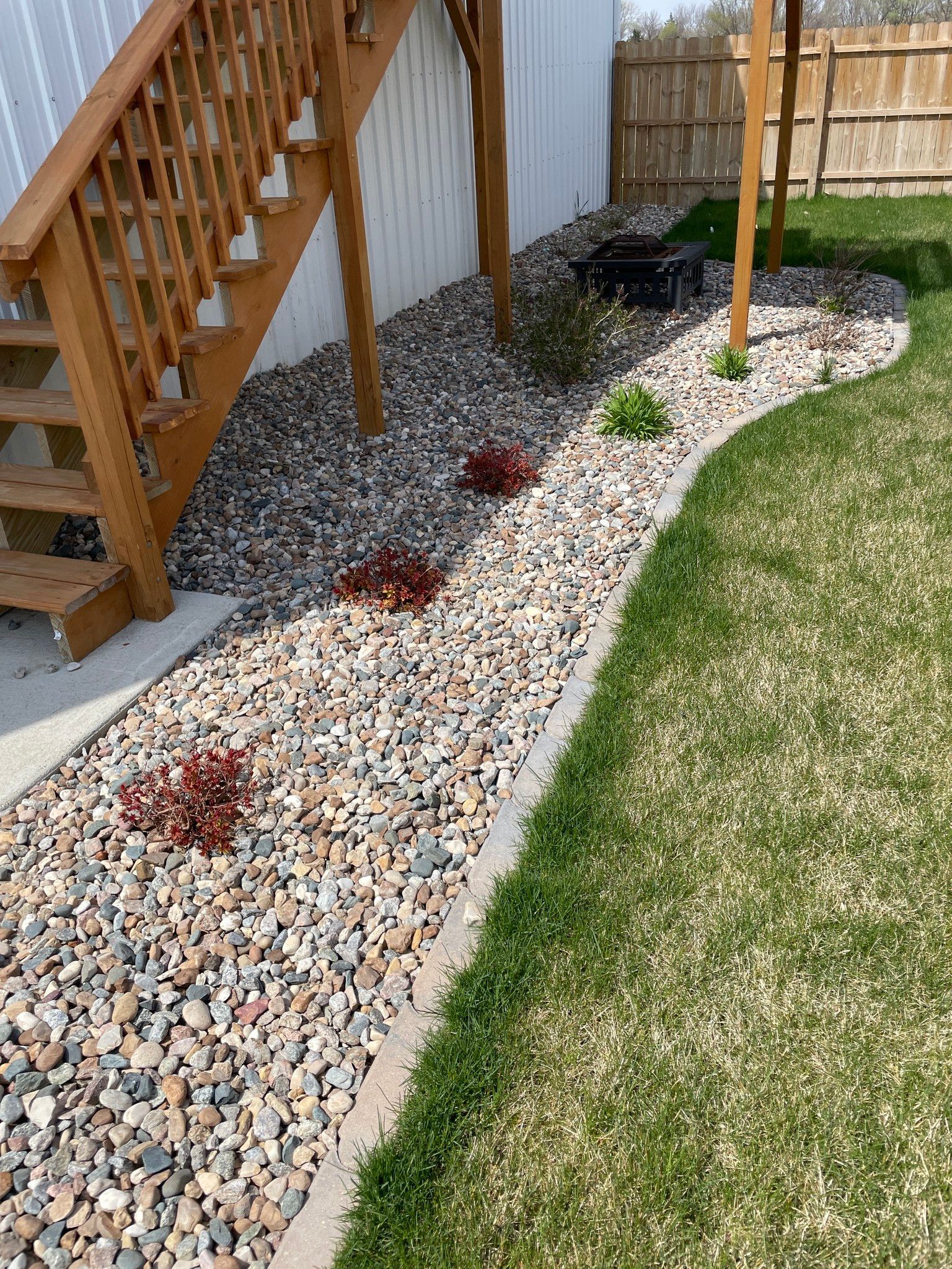 Curved white gravel border beside wooden stairs, with small red shrubs and green lawn.
