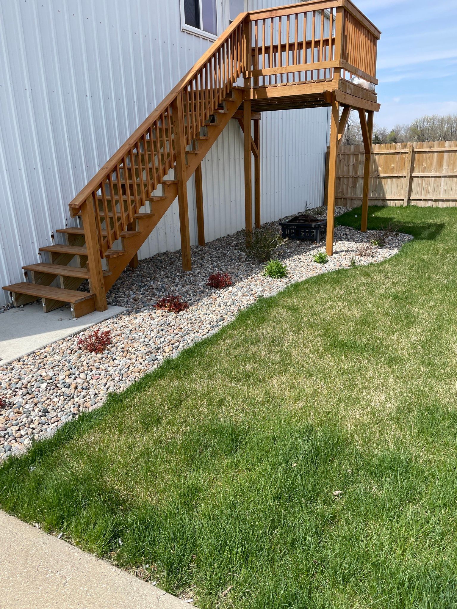Wooden exterior stairs and deck attached to a gray house beside a landscaped yard.