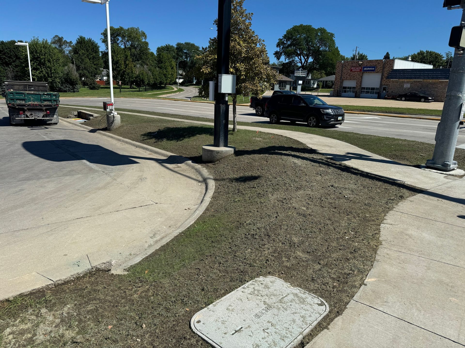 Sidewalk curb ramp beside a road and parking lot, with a grassy median and parked cars.
