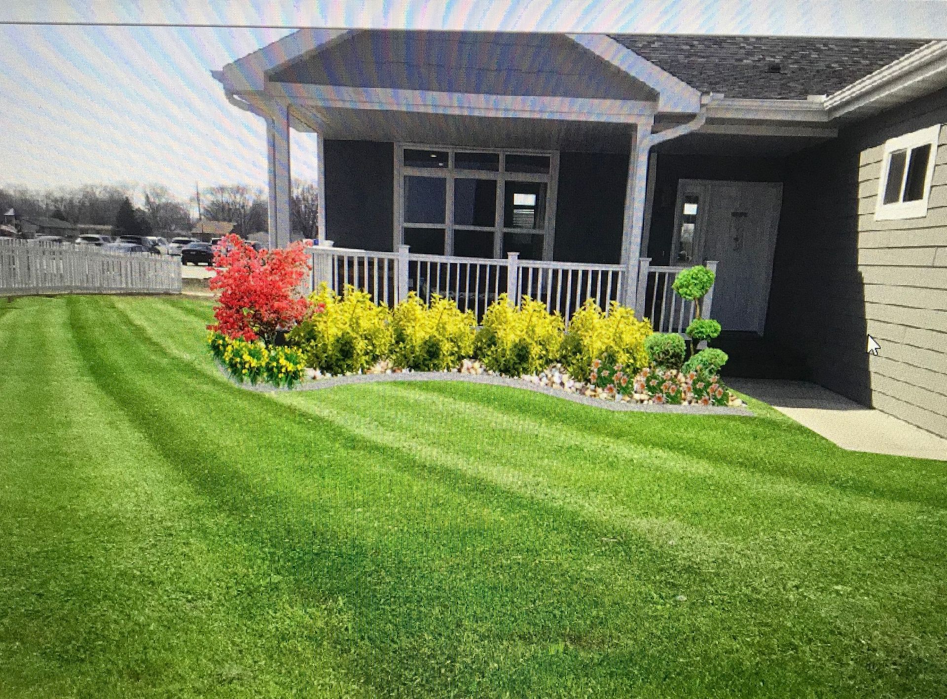 Front porch with black siding, white railing, and a landscaped lawn with red and yellow flowers.
