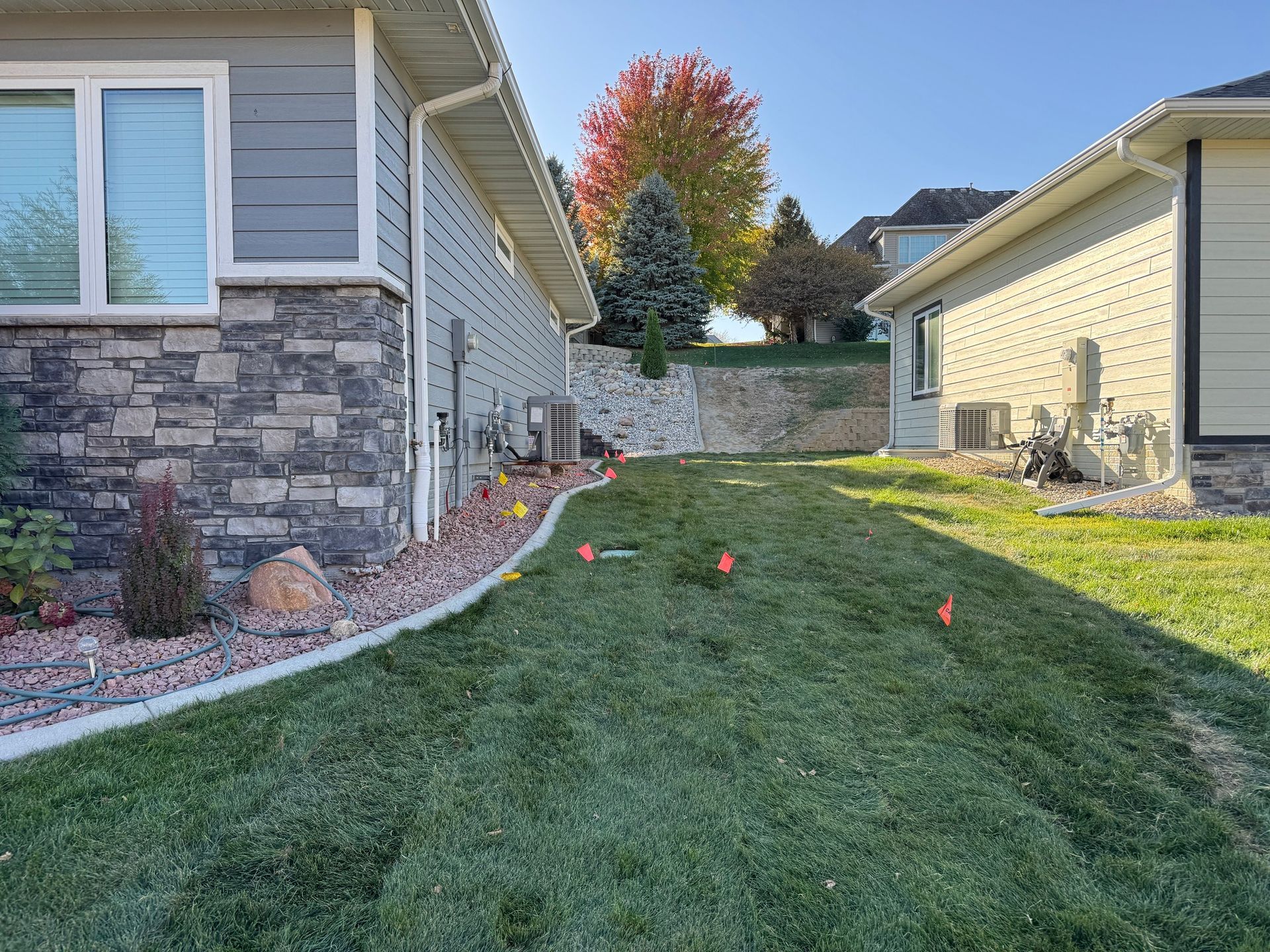 Narrow grass side yard between two houses, with stone edging and a colorful autumn tree in the background