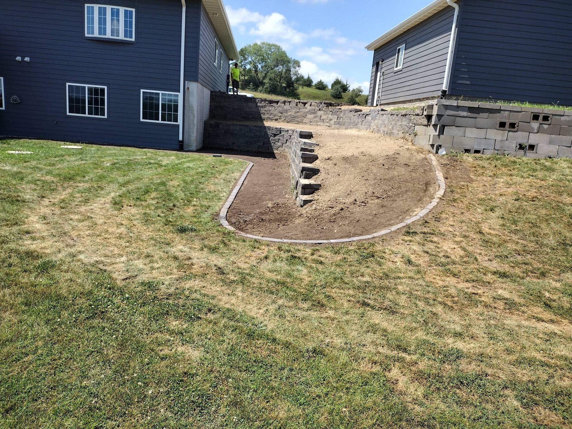 Backyard landscaping with a stone path and dirt mound between two houses under construction.