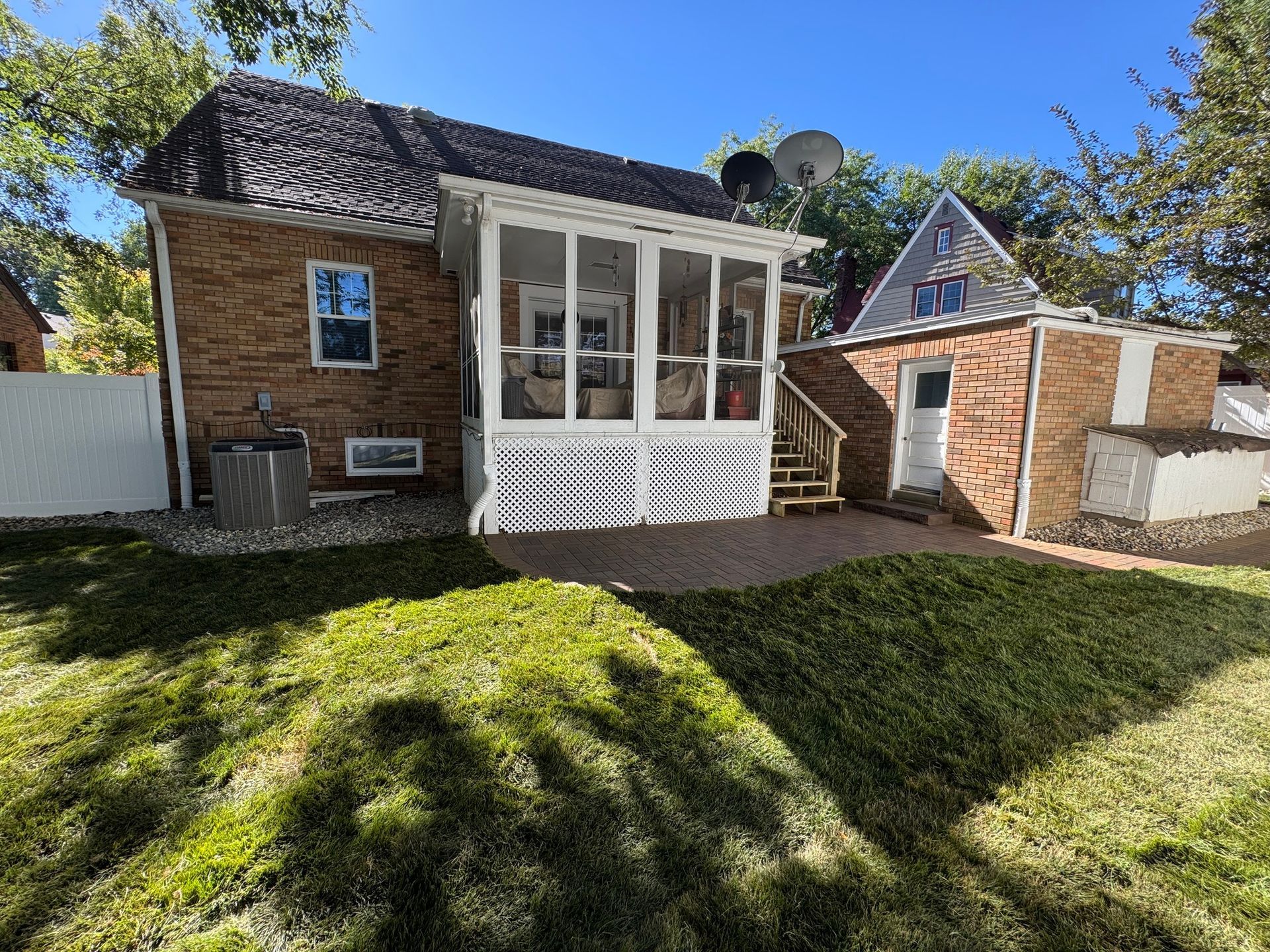 Small brick house with white porch and steep roof, set on a grassy yard in bright sunlight