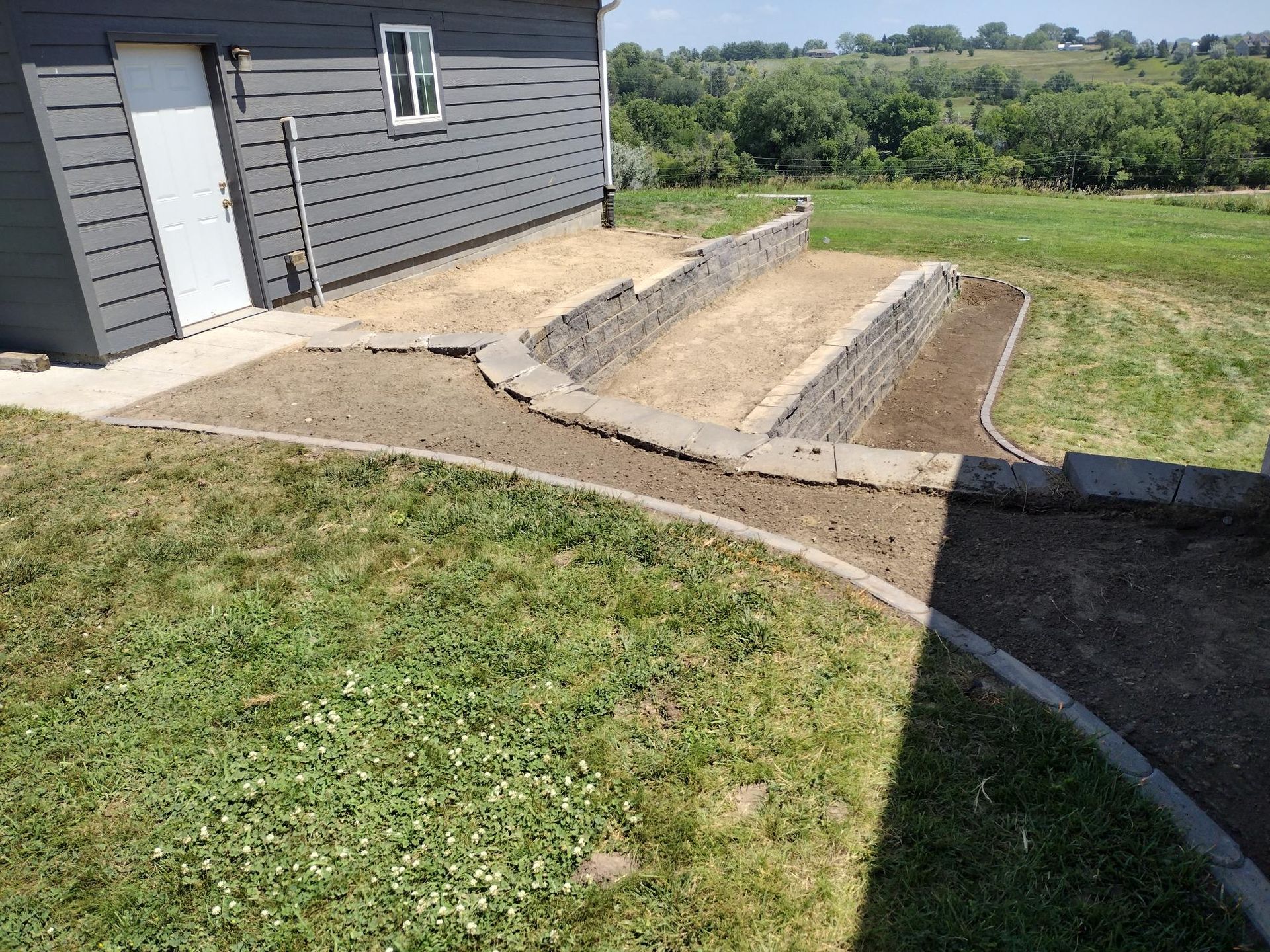 Backyard beside a gray house with a concrete ramp and steps leading down a grassy slope