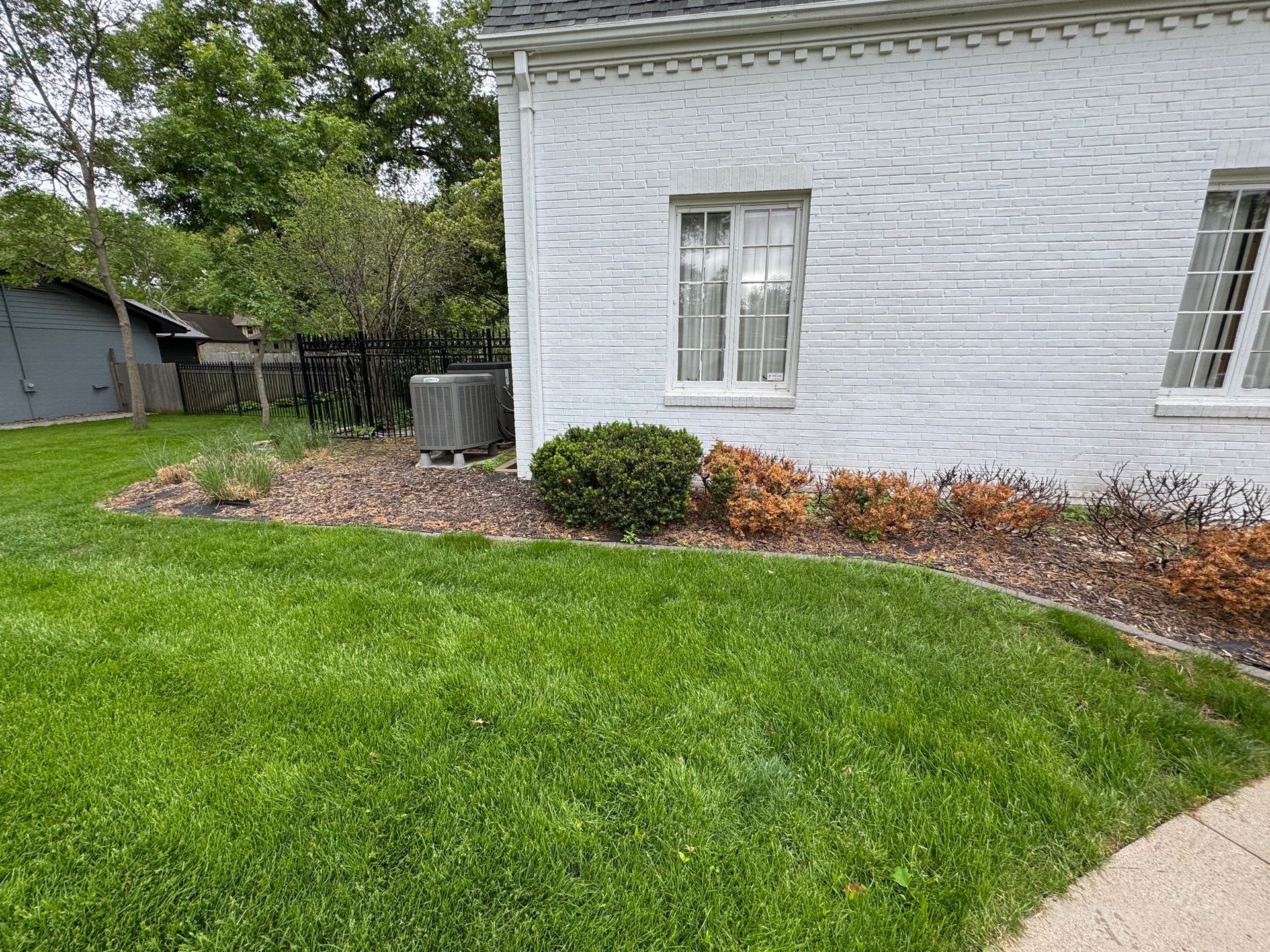 White house exterior with green lawn, mulched landscaping, and a curved walkway.