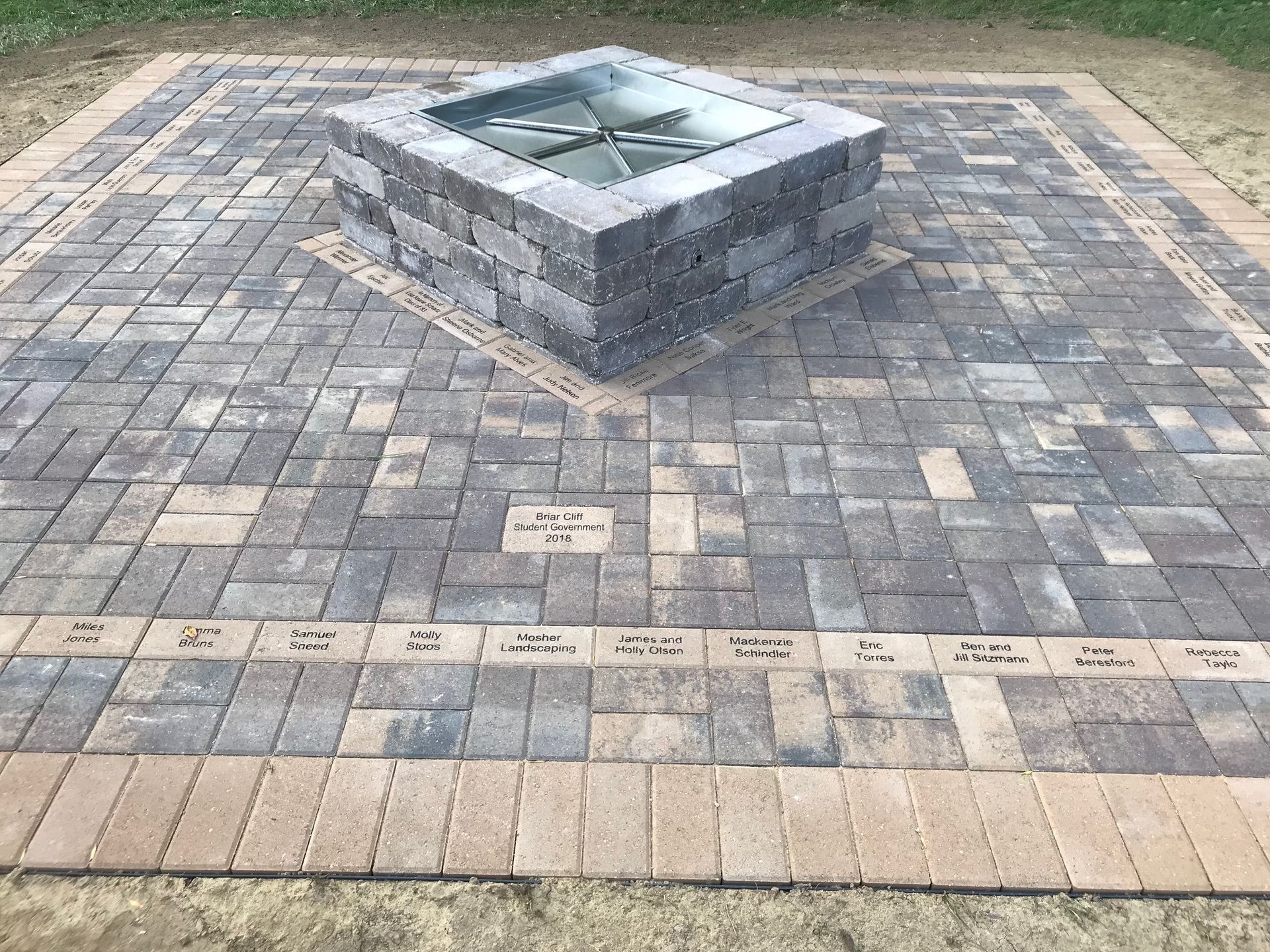 Stone memorial fountain set in a paved plaza with engraved bricks and a small plaque nearby