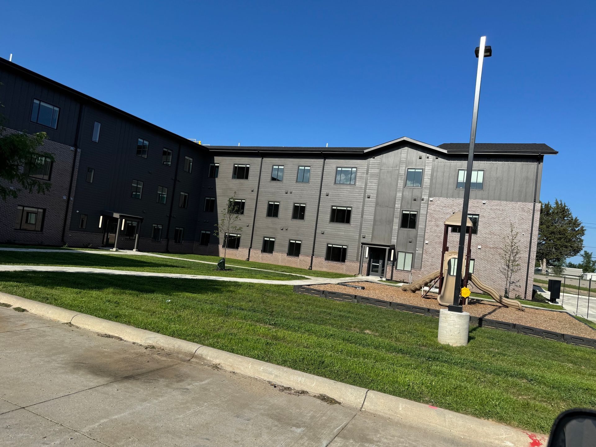 Modern apartment building with gray exterior, green lawn, and blue sky in front.