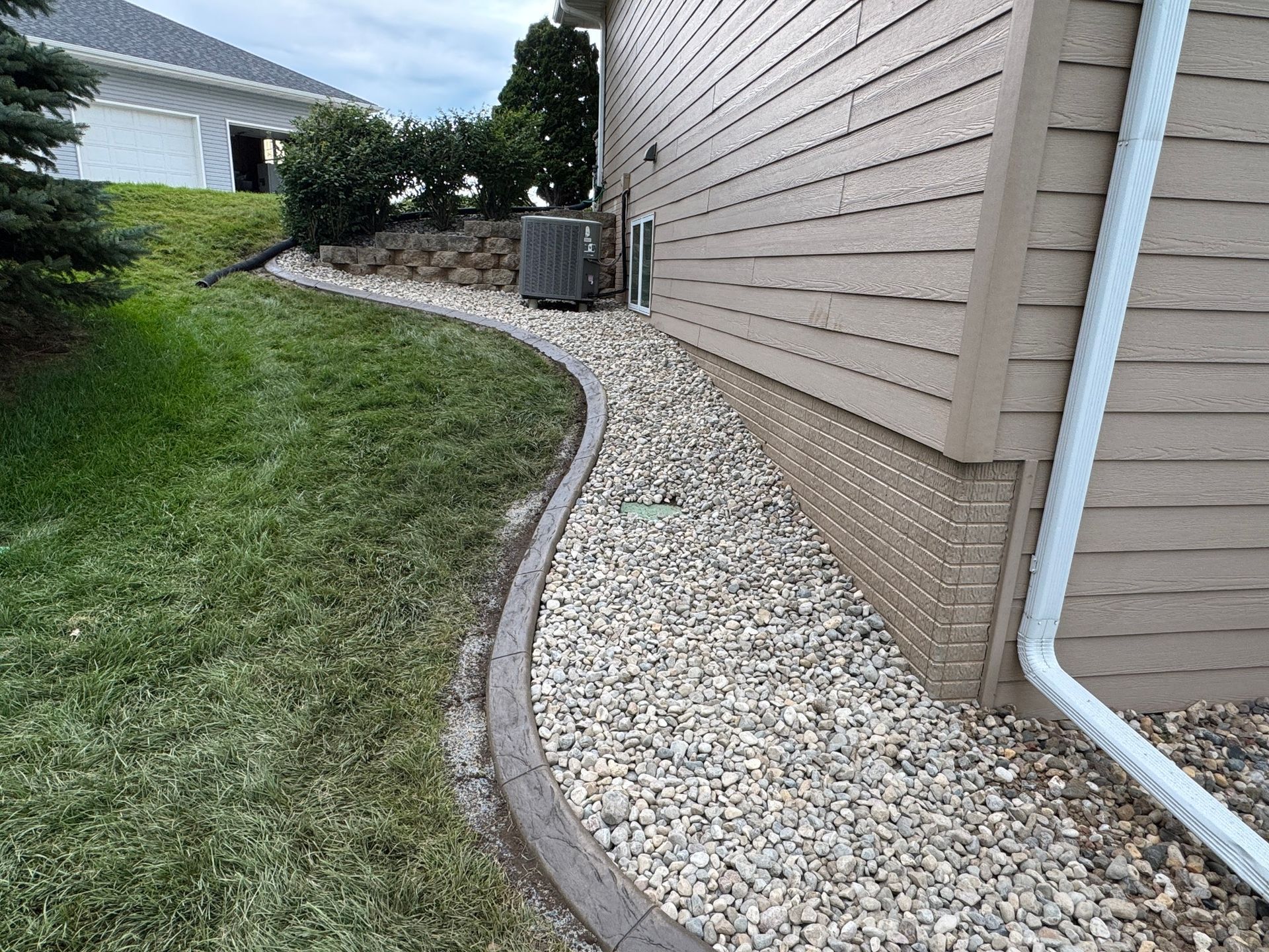Gravel drainage strip along a house foundation beside a curved lawn and landscaped yard