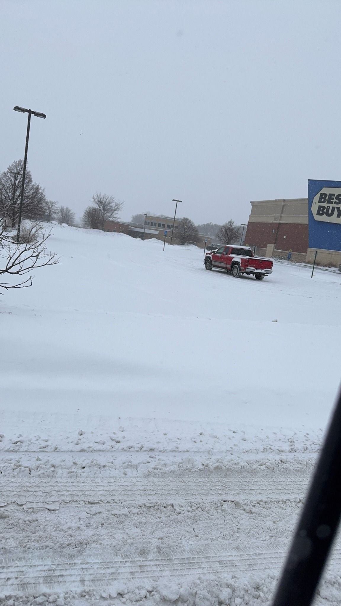 Snow-covered roadside with a red ATV beside a building under an overcast sky.