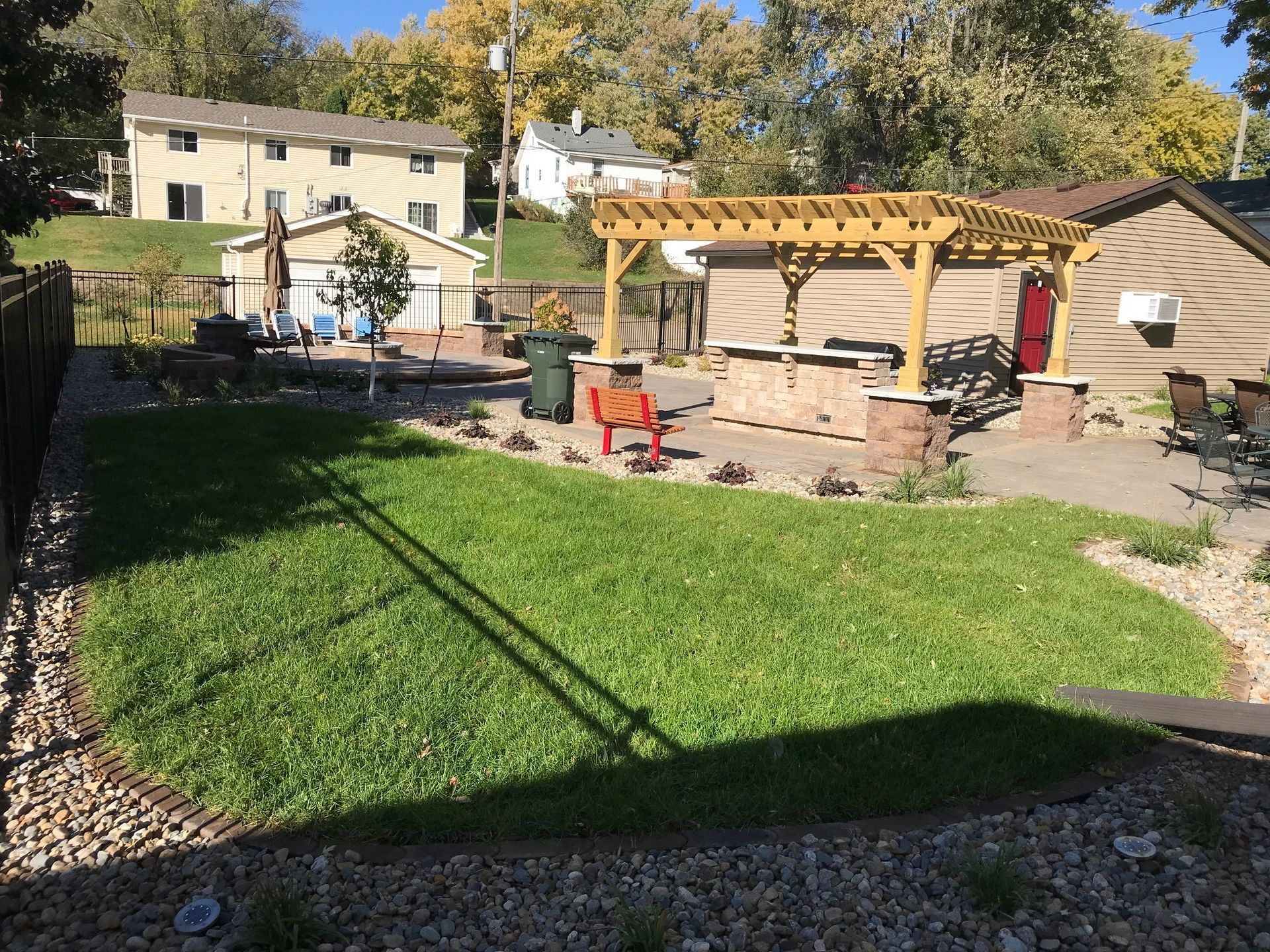 Backyard with green lawn, stone patio, pergola, and outdoor seating in bright sunlight