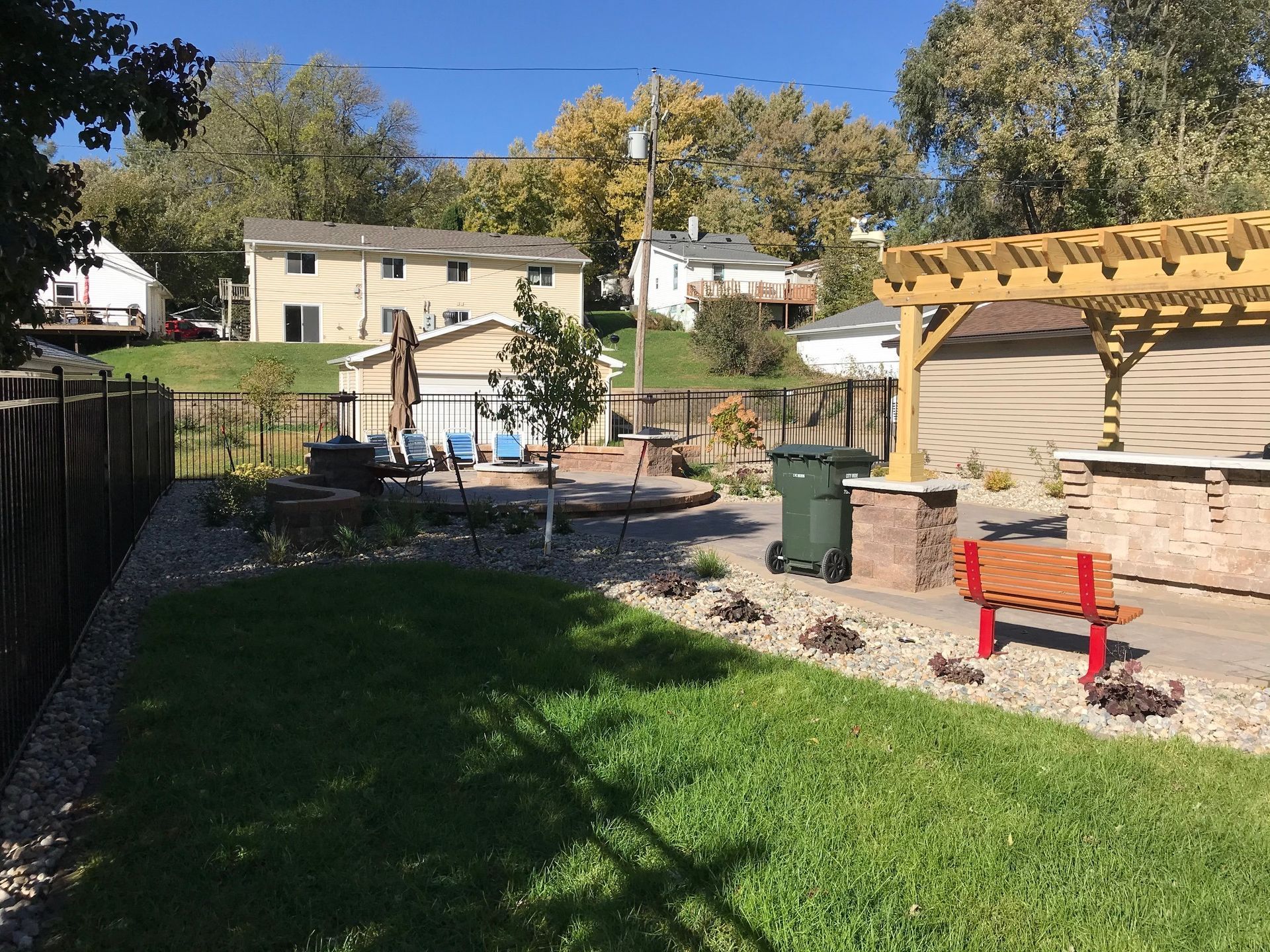 Backyard with green lawn, patio pergola, red bench, and small raised garden beds