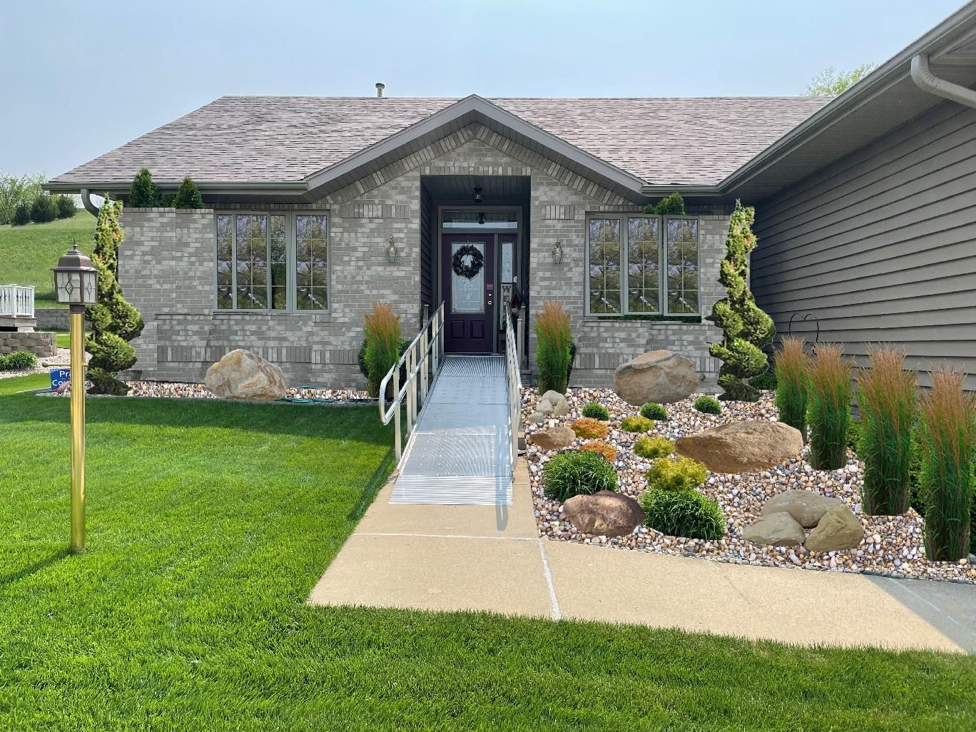 Single-story stone house with ramped walkway, front garden, and manicured lawn under a gray roof.