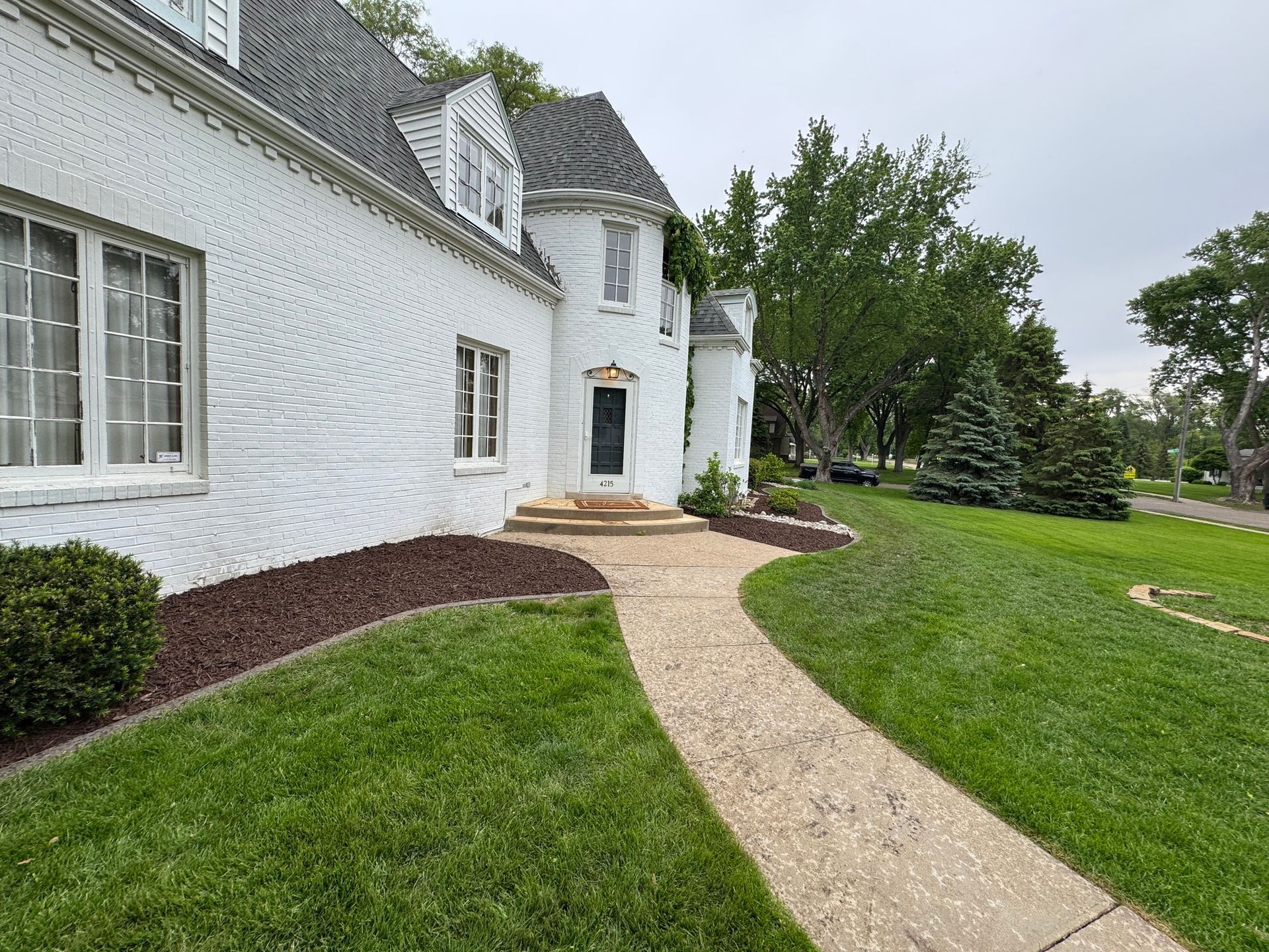 White house with curved gravel path, green lawn, and trees on an overcast day