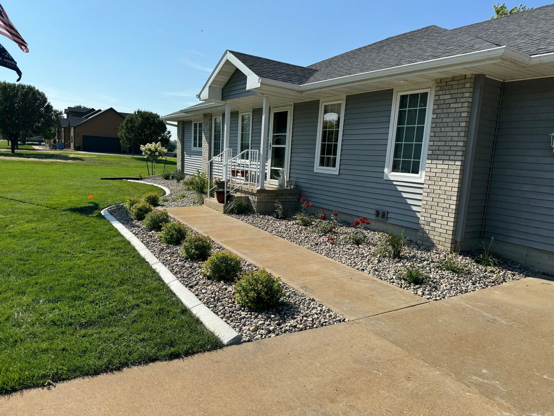 Suburban house with gray siding, front porch, flower bed, and a curved concrete walkway