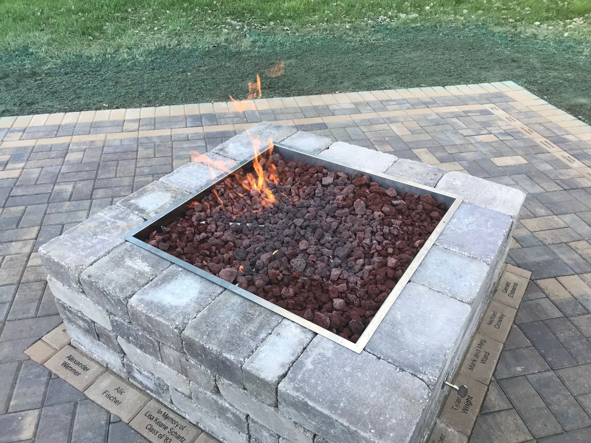 Stone fire pit with a small flame burning in a paved outdoor patio area