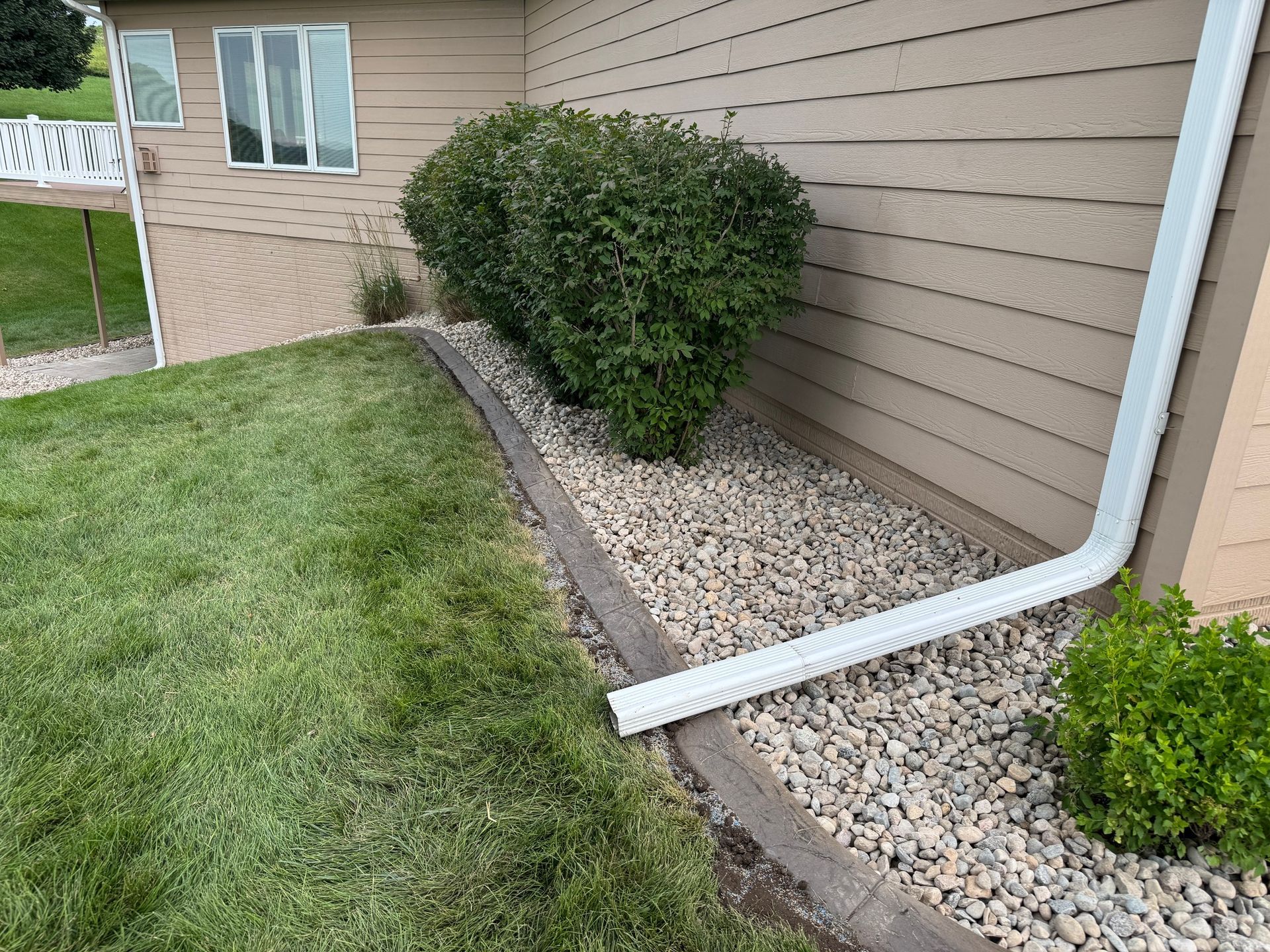 Landscaped yard with gravel bed, trimmed shrubs, and tan house siding next to a lawn