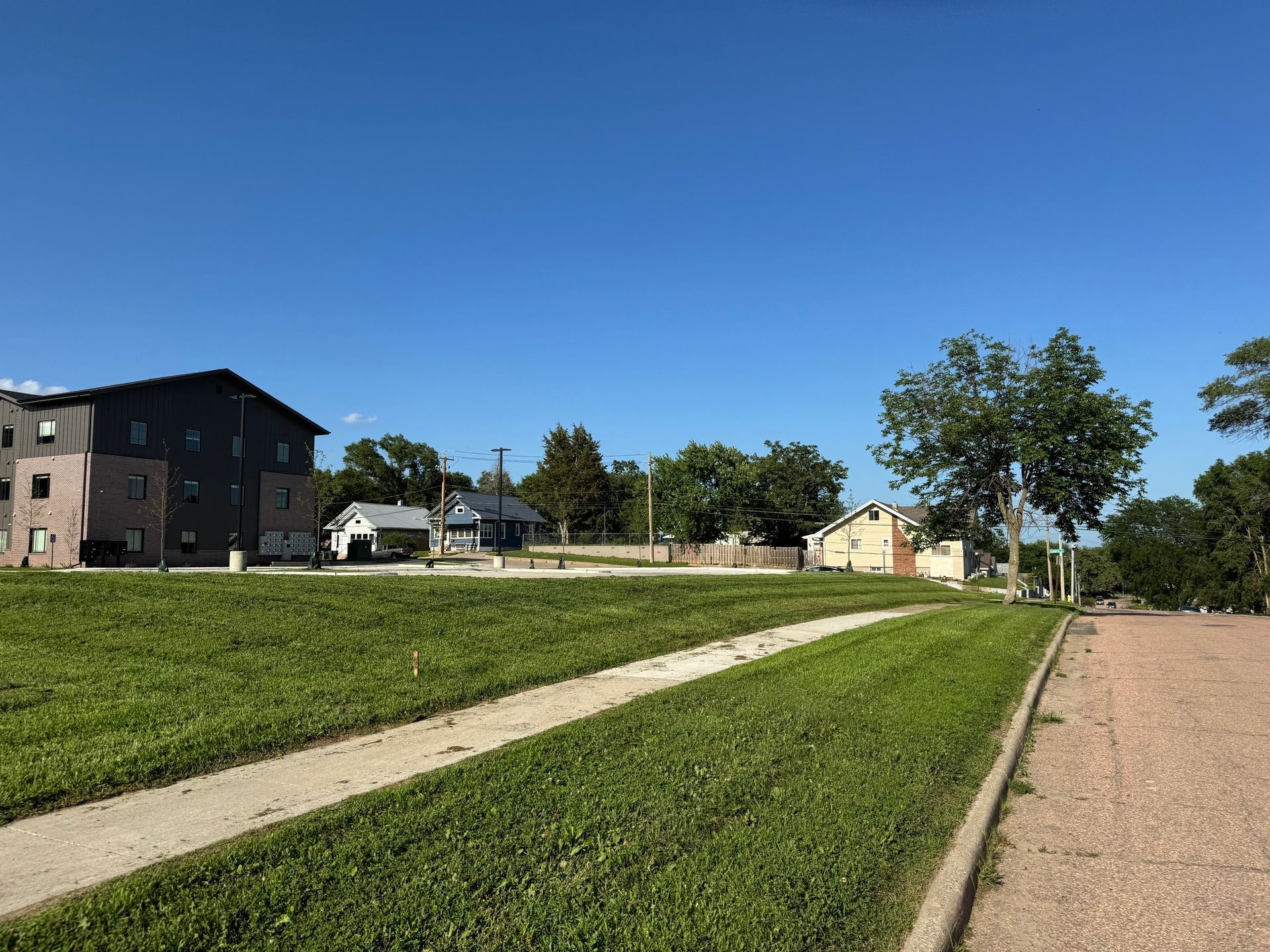 Grassy park path beside apartment buildings under a clear blue sky