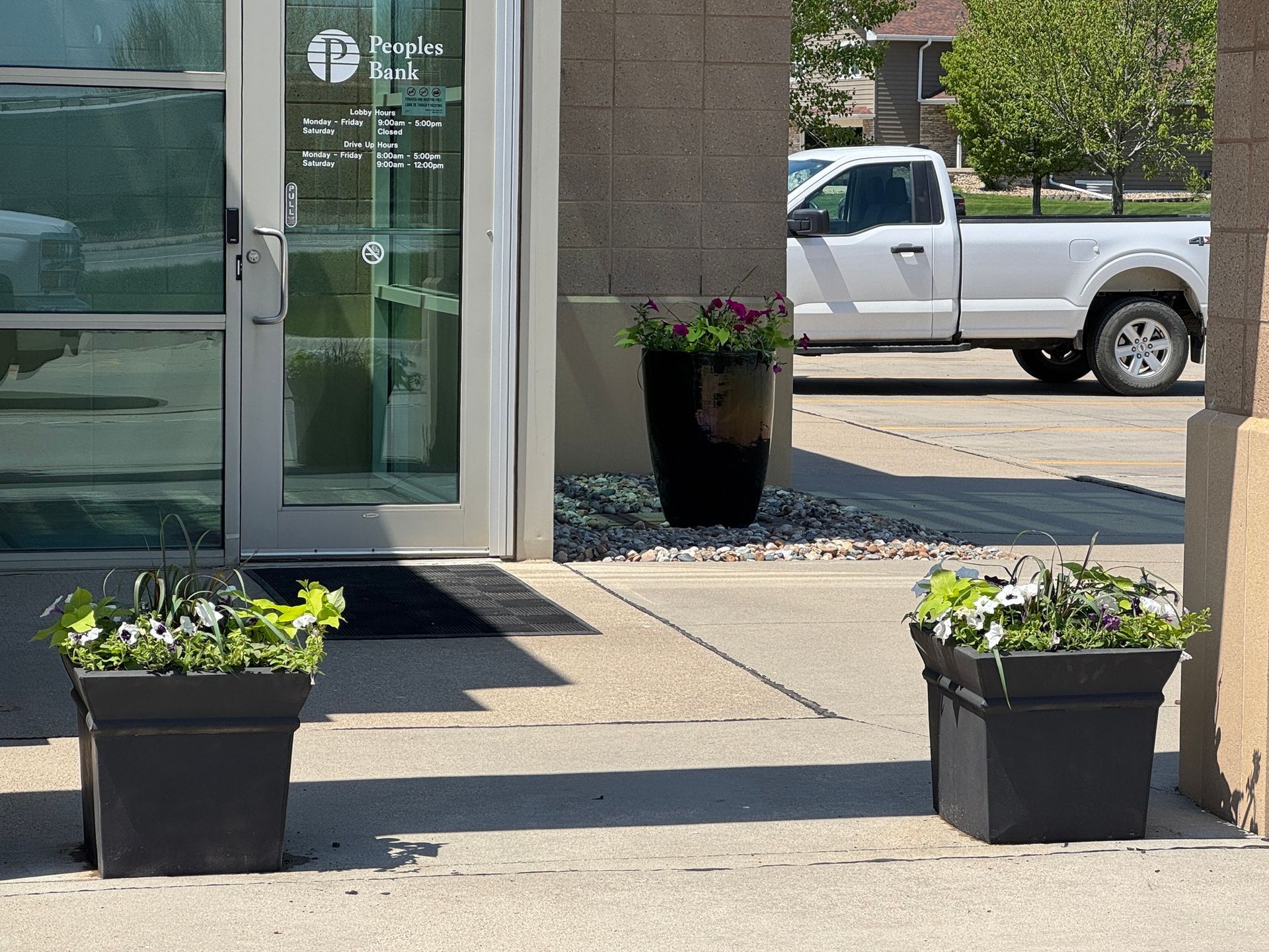 Entrance of a building with two black planters and a white pickup truck in the background