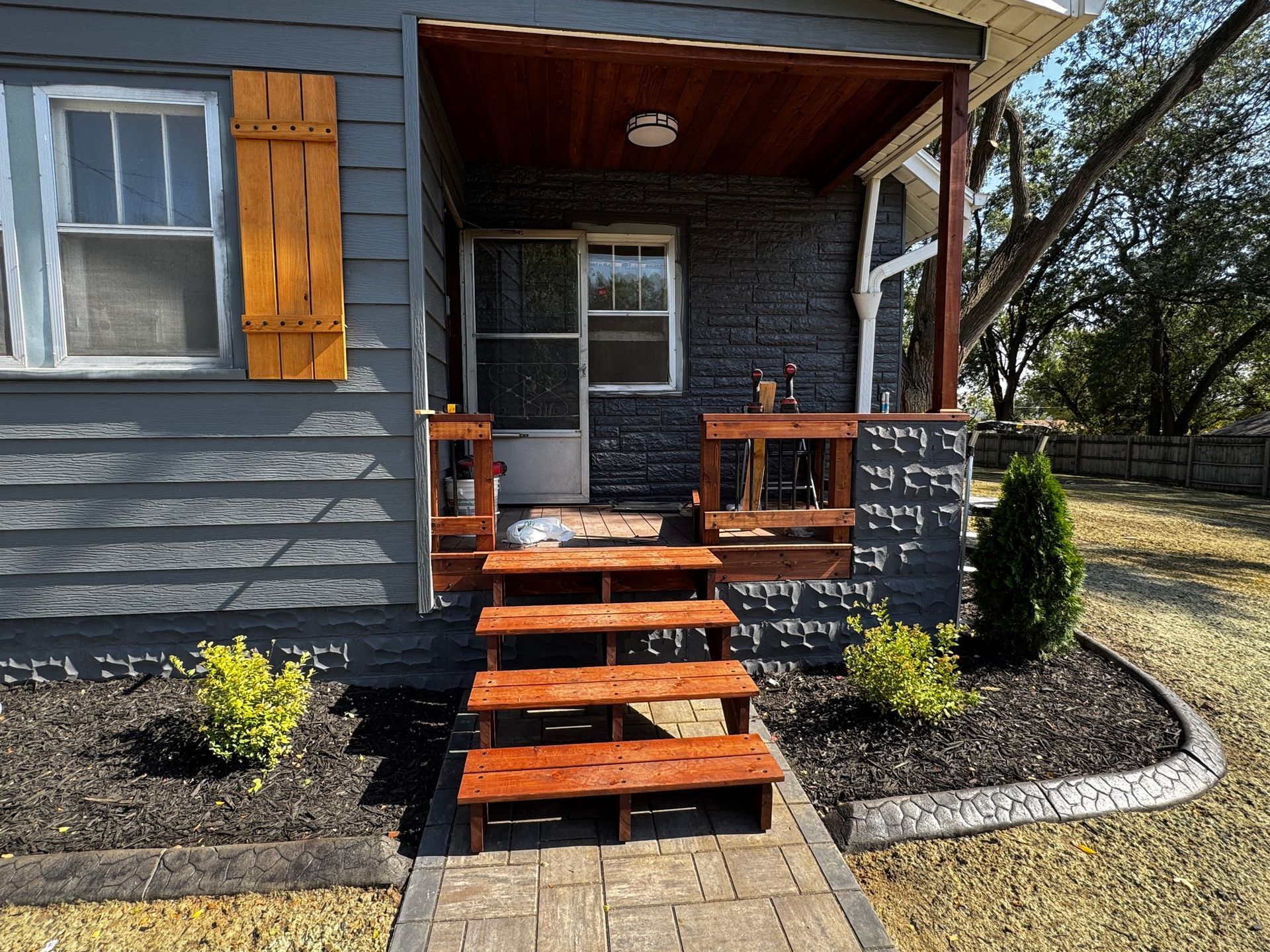 Front porch of a gray house with orange steps, black railings, and two small shrubs in a landscaped yard