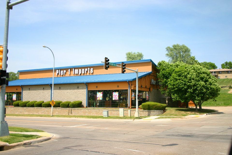 Corner street view of a low brick building with a blue roof sign, traffic light, and trees