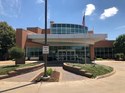 Front entrance of a modern building with glass doors, brick walls, and an American flag under a blue sky.