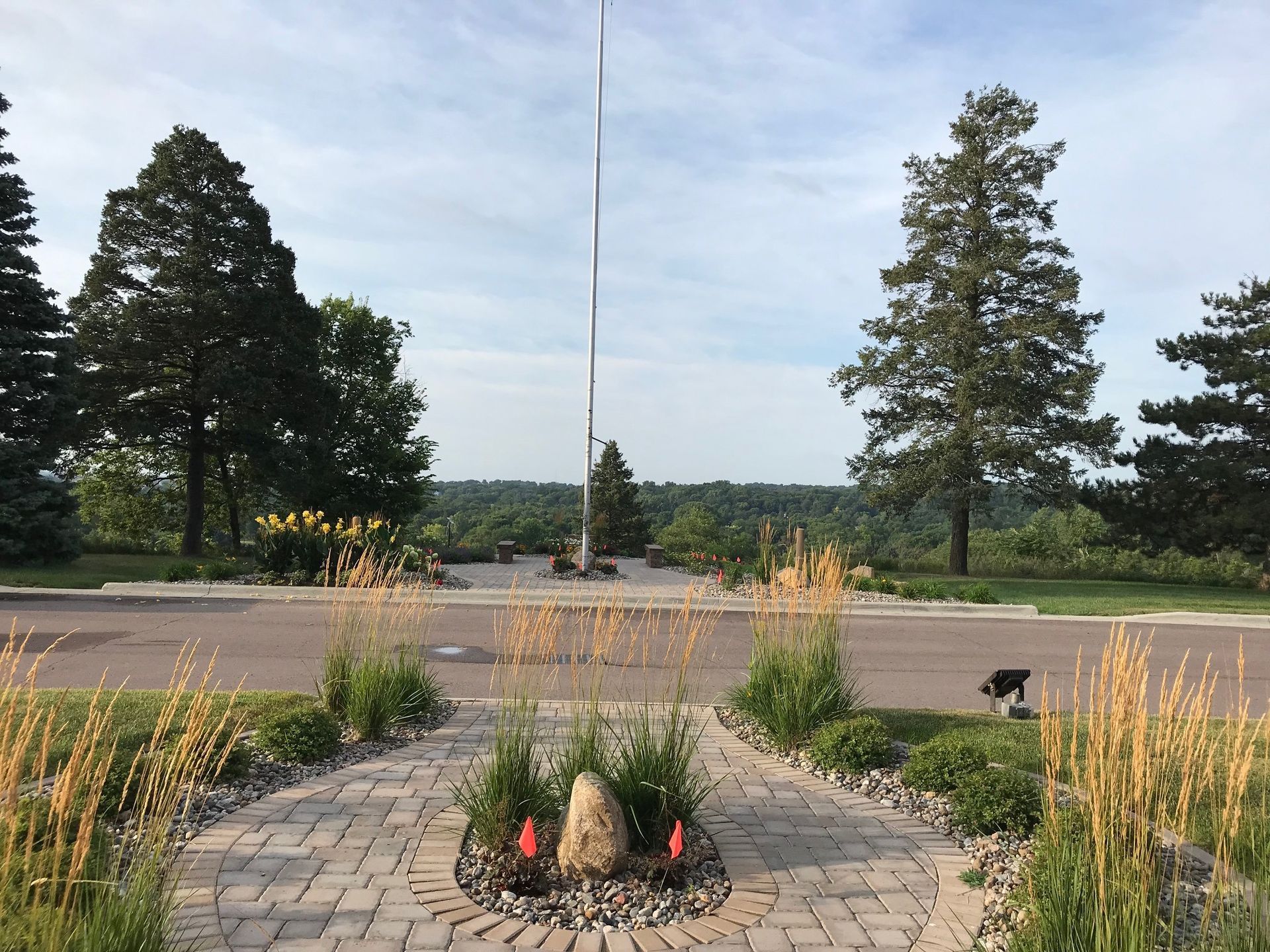 Brick patio garden with circular fountain, tall grasses, and trees under a cloudy sky