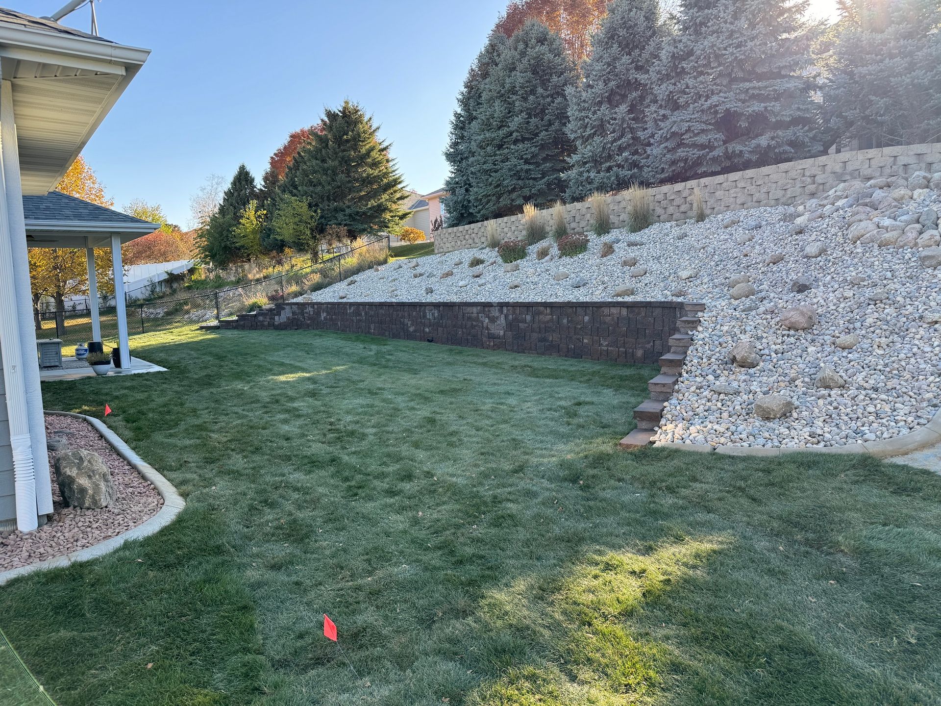 Backyard lawn beside a stone retaining wall and landscaped shrubs in autumn light