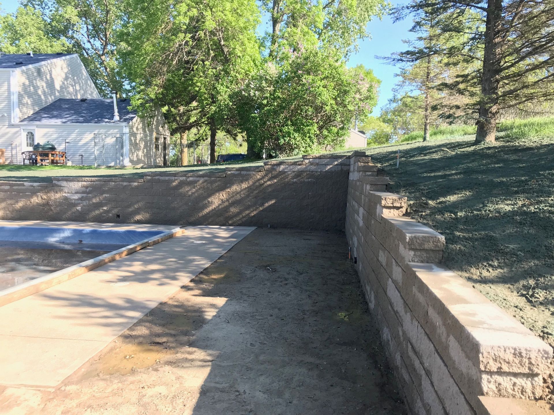 Residential driveway with a low stone retaining wall, trees, and a house in the background