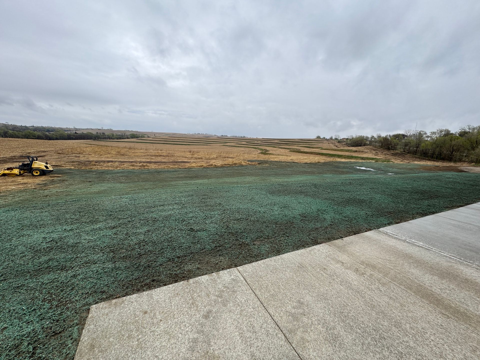 New concrete walkway beside a green-covered field under a cloudy sky