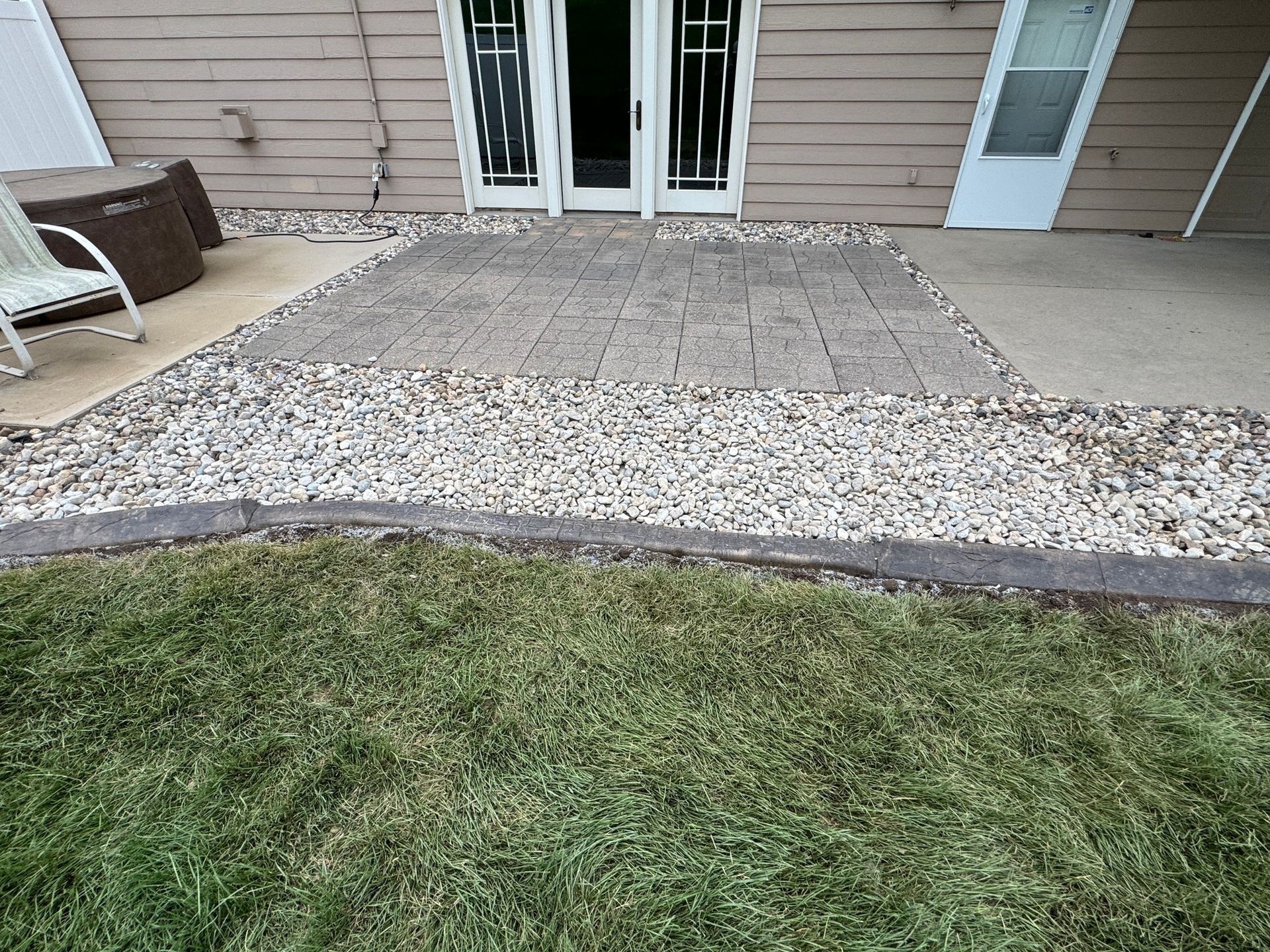Gravel patio bordered by grass in front of a beige house with white French doors.