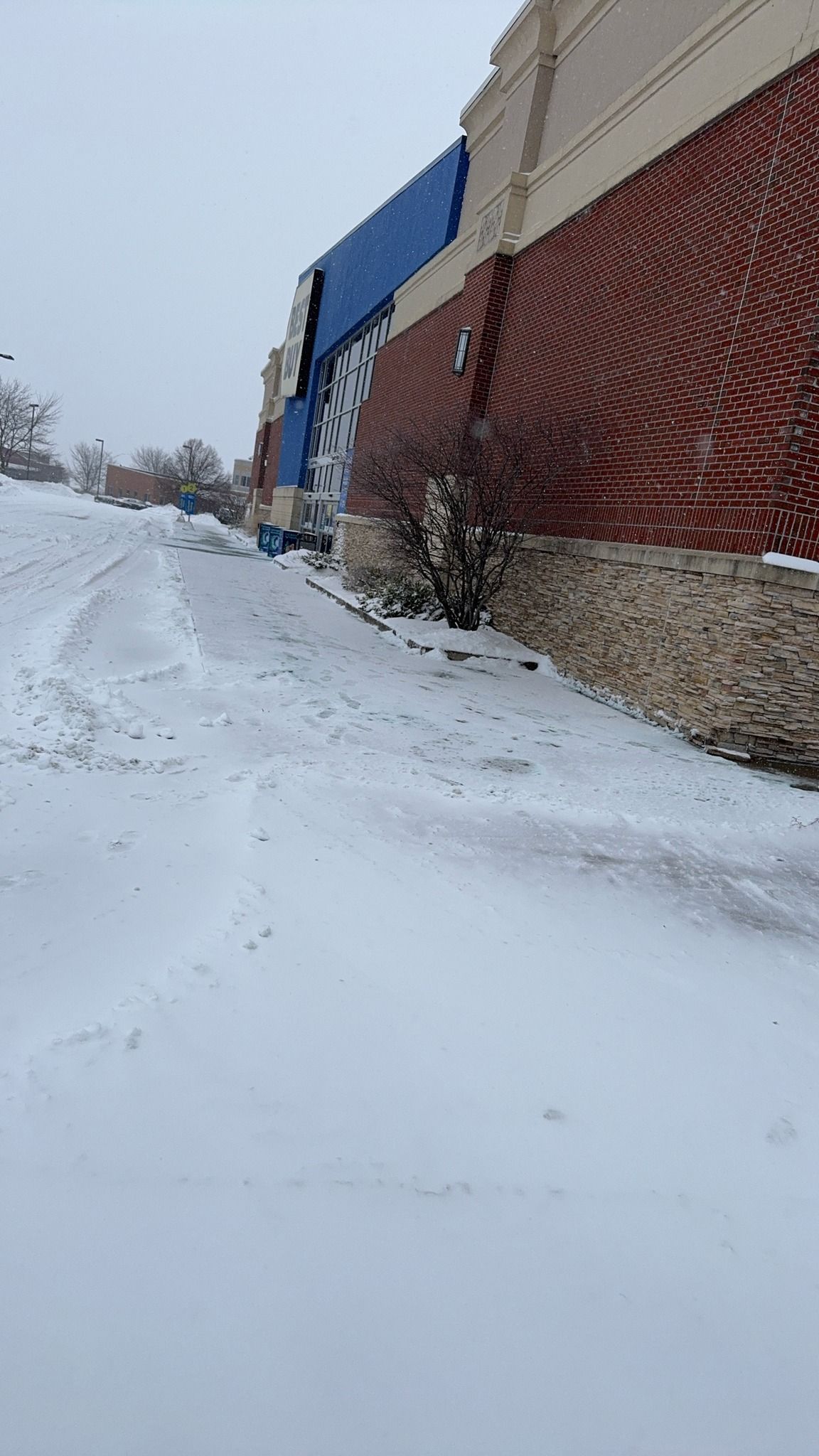Snow-covered sidewalk beside a red brick building with blue awnings on a winter day