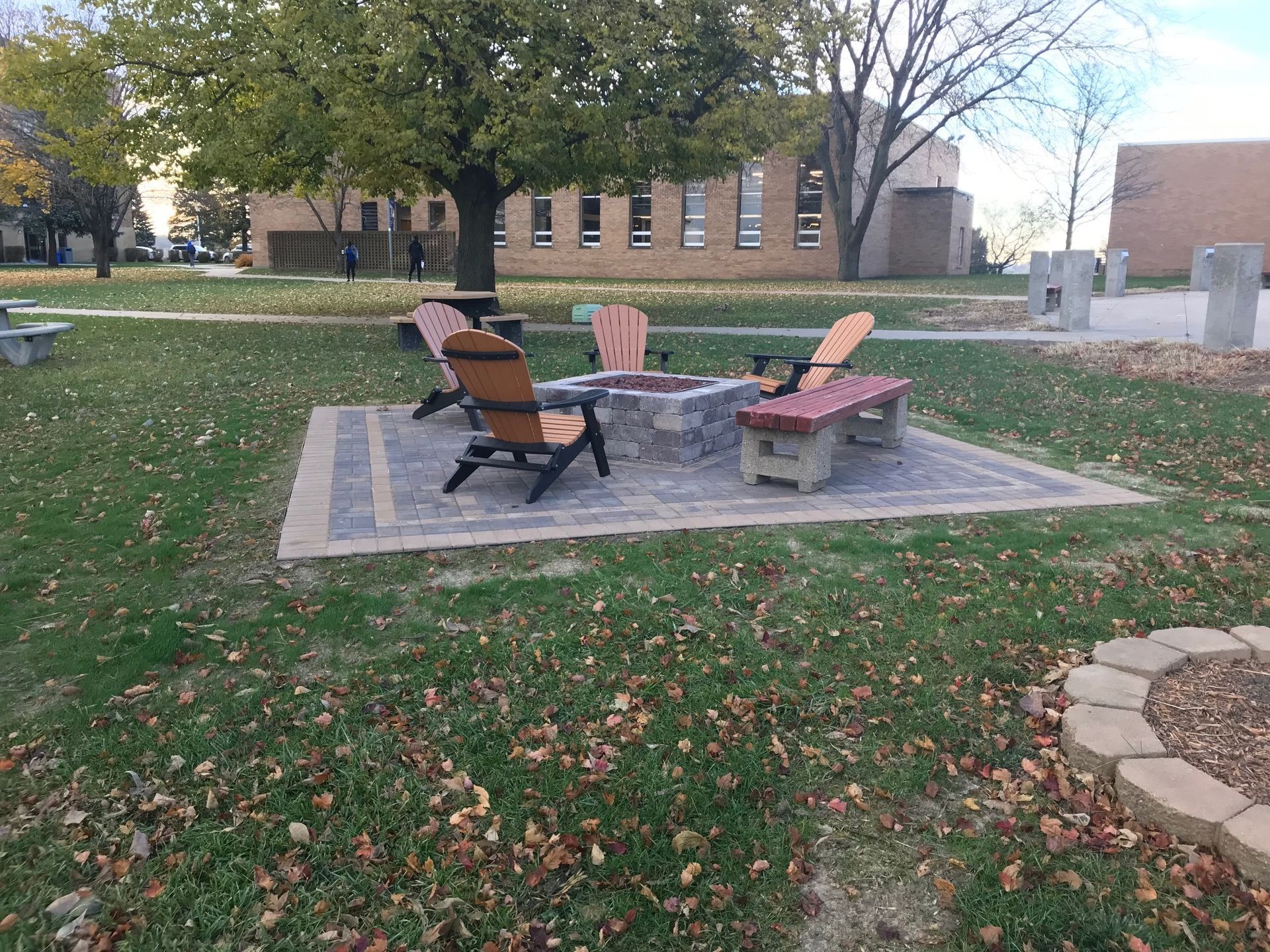 Outdoor fire pit area with two chairs on a paved pad in a grassy courtyard.