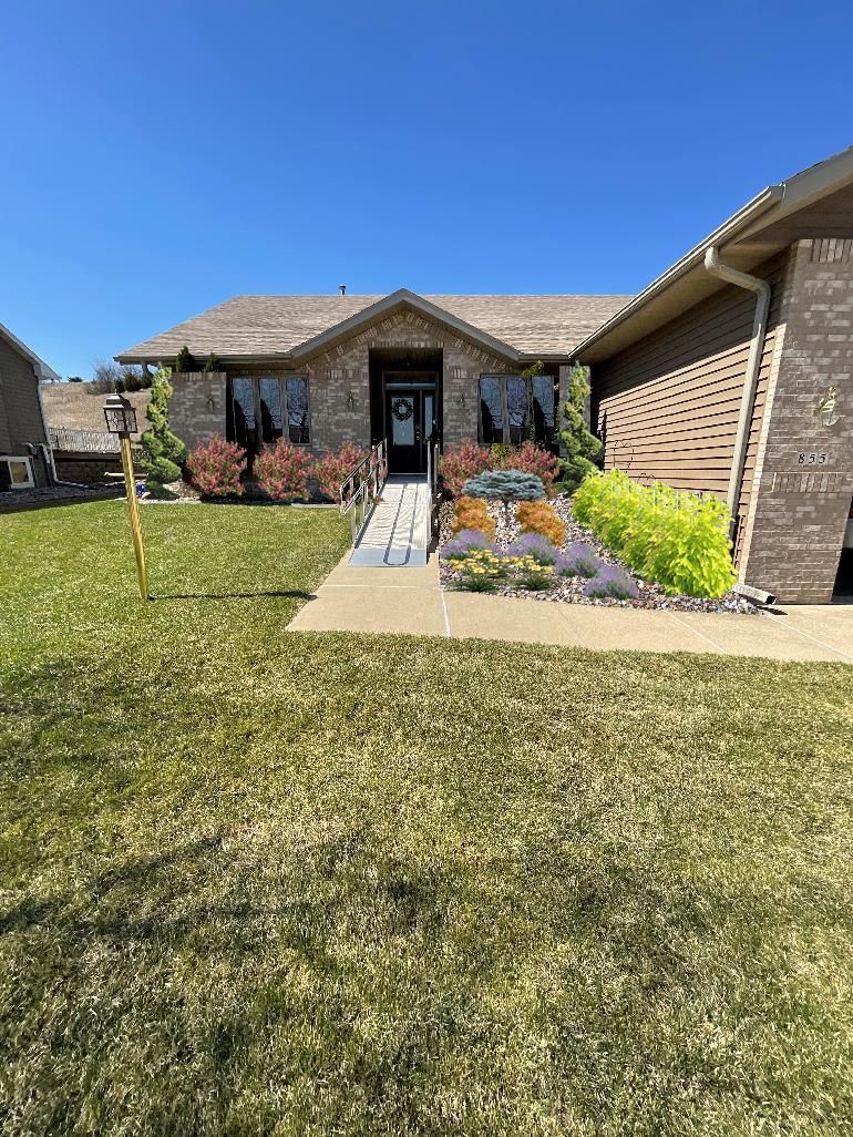Front yard of a brick house with a walkway, flower beds, and a clear blue sky.