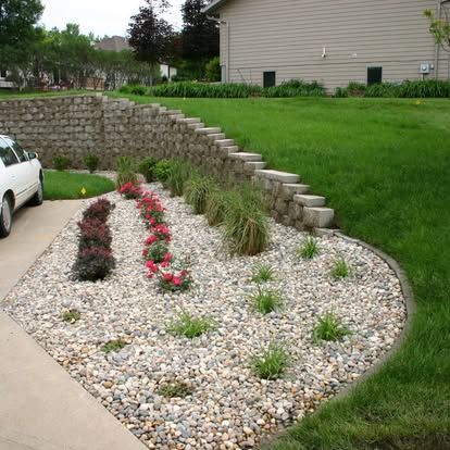 Curved gravel flower bed with pink flowers and grass beside a retaining wall and house lawn