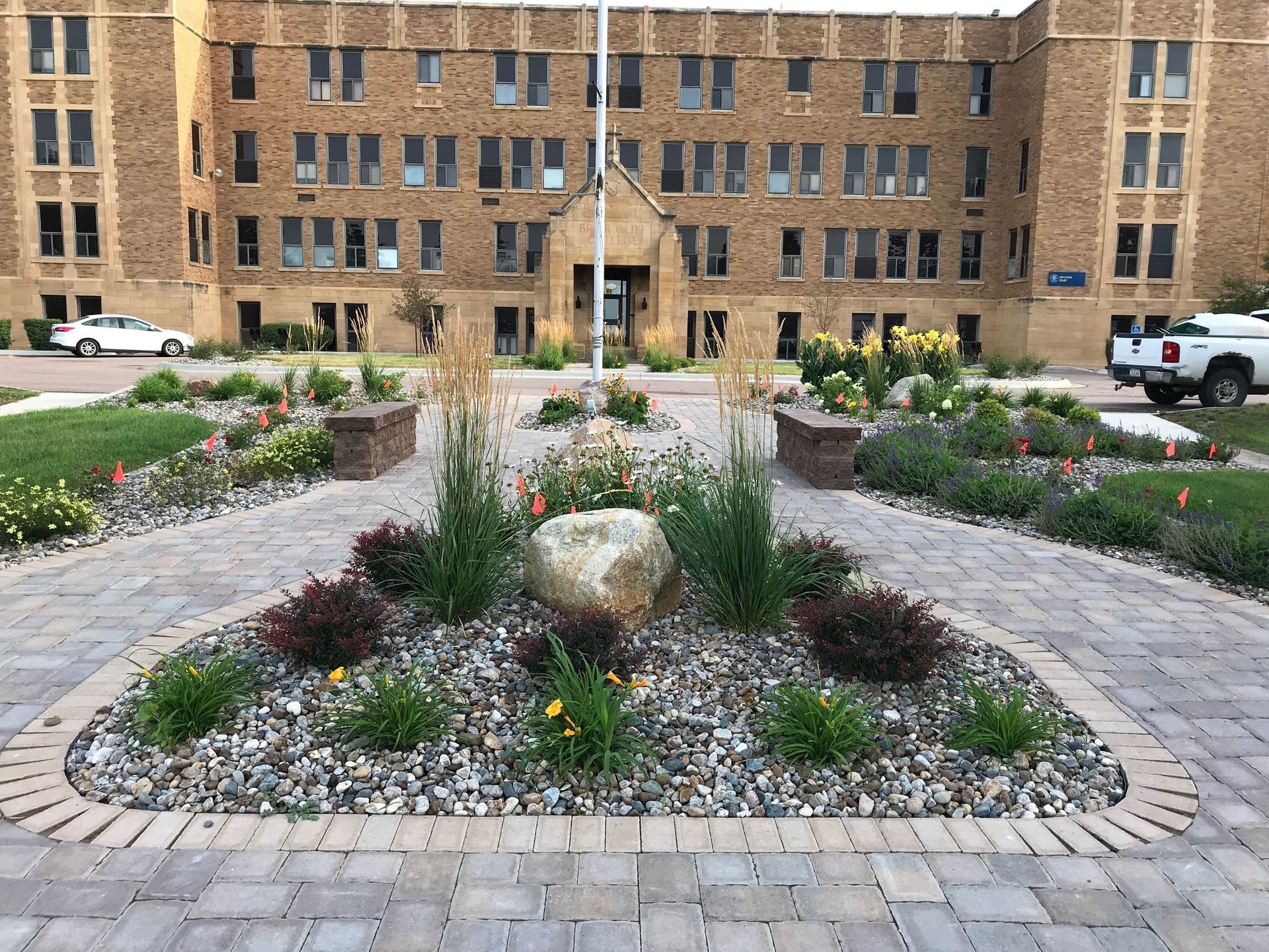 Circular flower bed with rocks and pink blooms in a brick courtyard in front of an apartment building