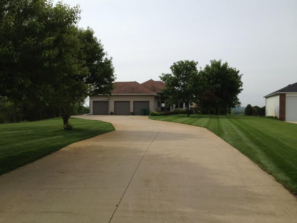 Long driveway leading to a suburban house with two garage doors and green lawns on both sides