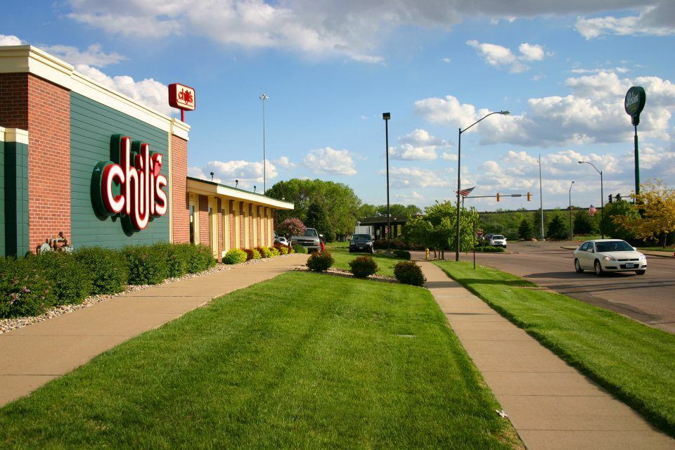 Crate and Barrel storefront with manicured lawn, sidewalk, and parking lot under a blue sky