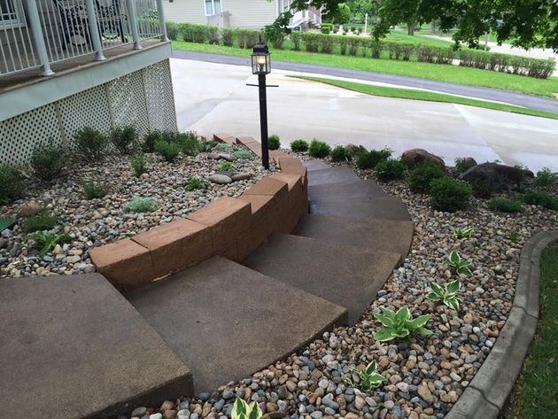 Curved concrete walkway with a low brick wall, garden beds, and a lamp post beside a road