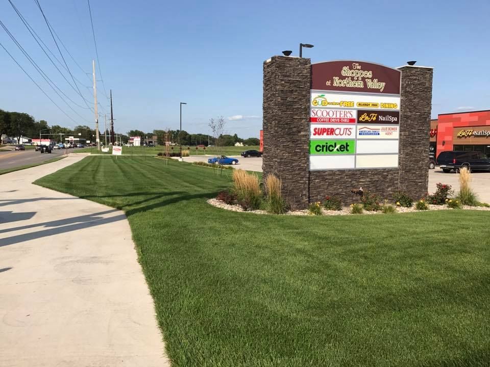 Shopping plaza sign beside a sidewalk and road on a sunny day