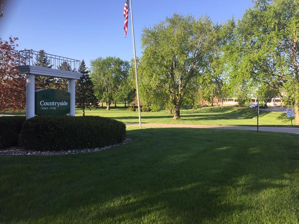 College campus sign on a landscaped lawn with trees, flagpole, and buildings in the background