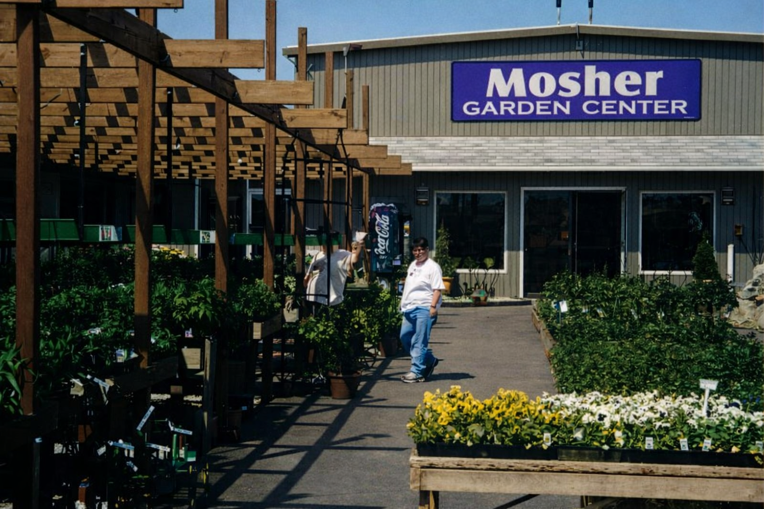Mosher Garden Center storefront with plants and flowers outside, and a person walking nearby