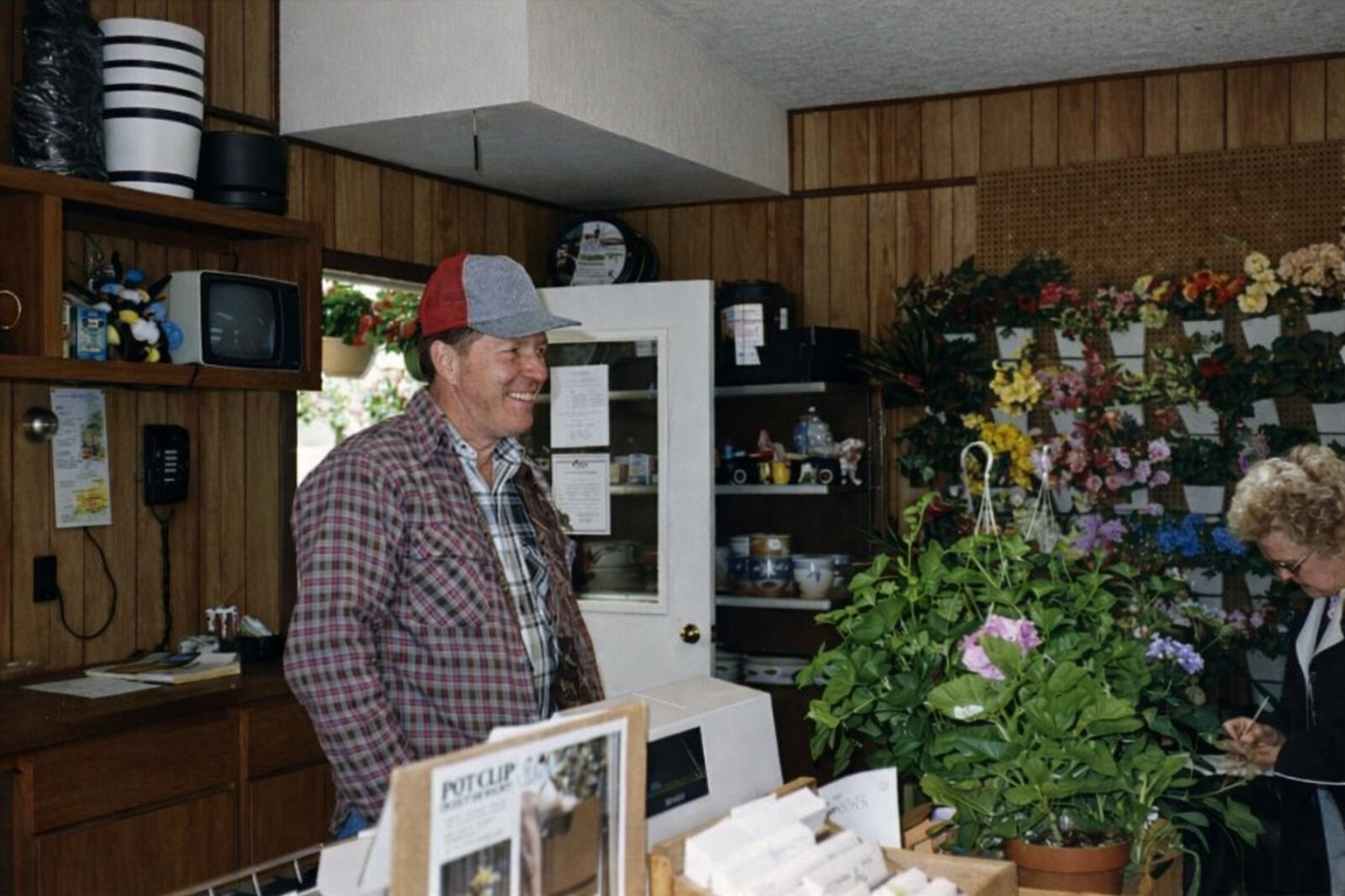 Flower shop counter with a man in a cap standing beside bouquets and shelves of vases