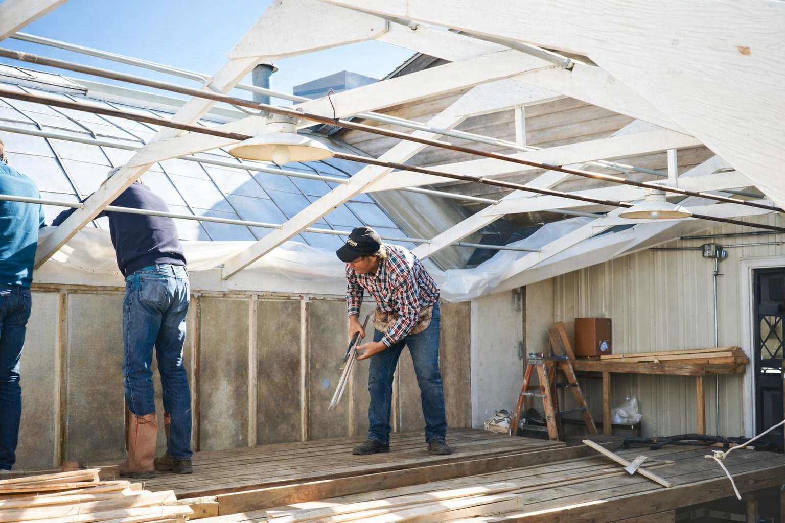 Workers repairing a damaged ceiling in a cluttered room with exposed beams and debris on the floor